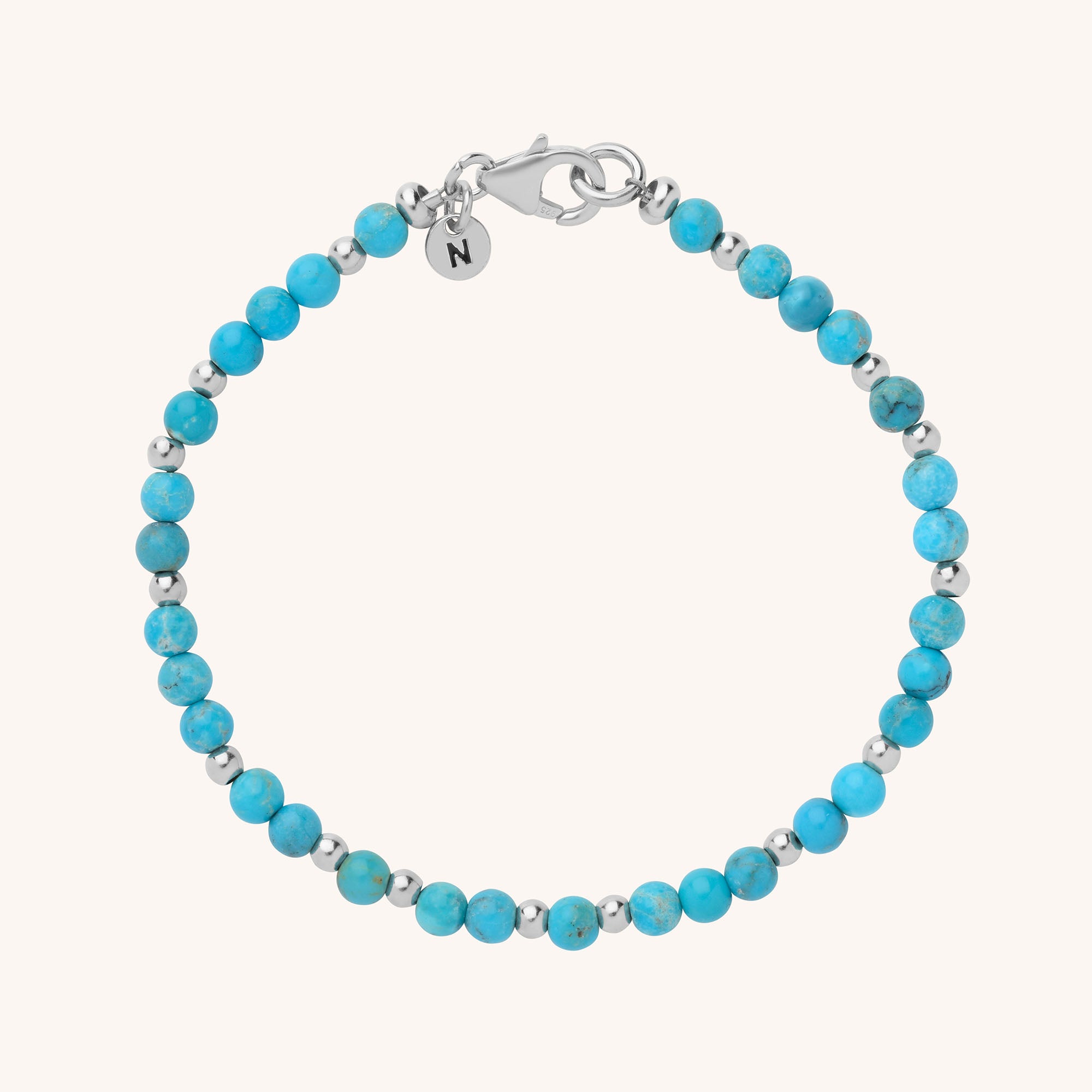 The Jewel Bead Birthstone Bracelet features alternating turquoise and silver beads, a silver lobster clasp, and a round charm engraved with the letter N—perfect as handmade jewellery or a unique personalized birthstone gift.
