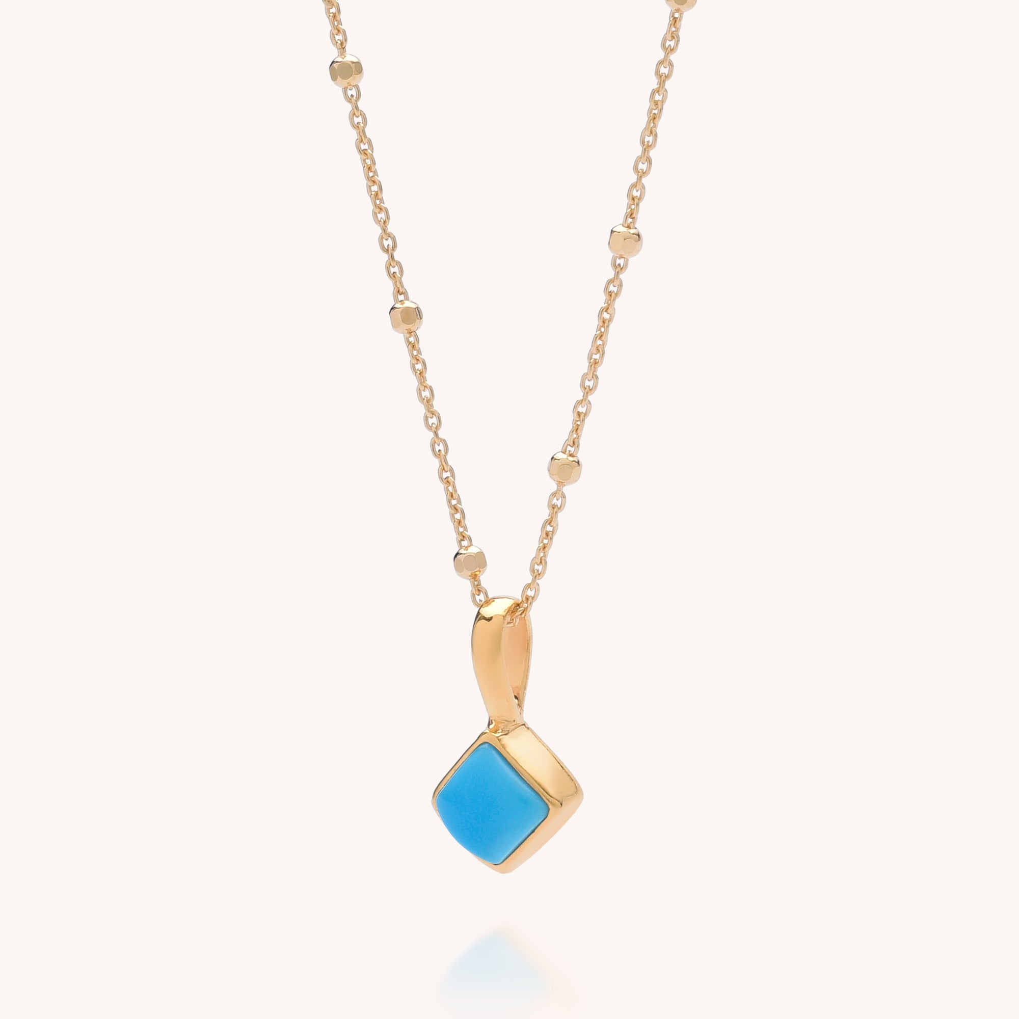 The Diamond Birthstone Necklace December features a gold chain with small round beads and a square turquoise pendant set in gold, cherished for its unique color and healing properties.