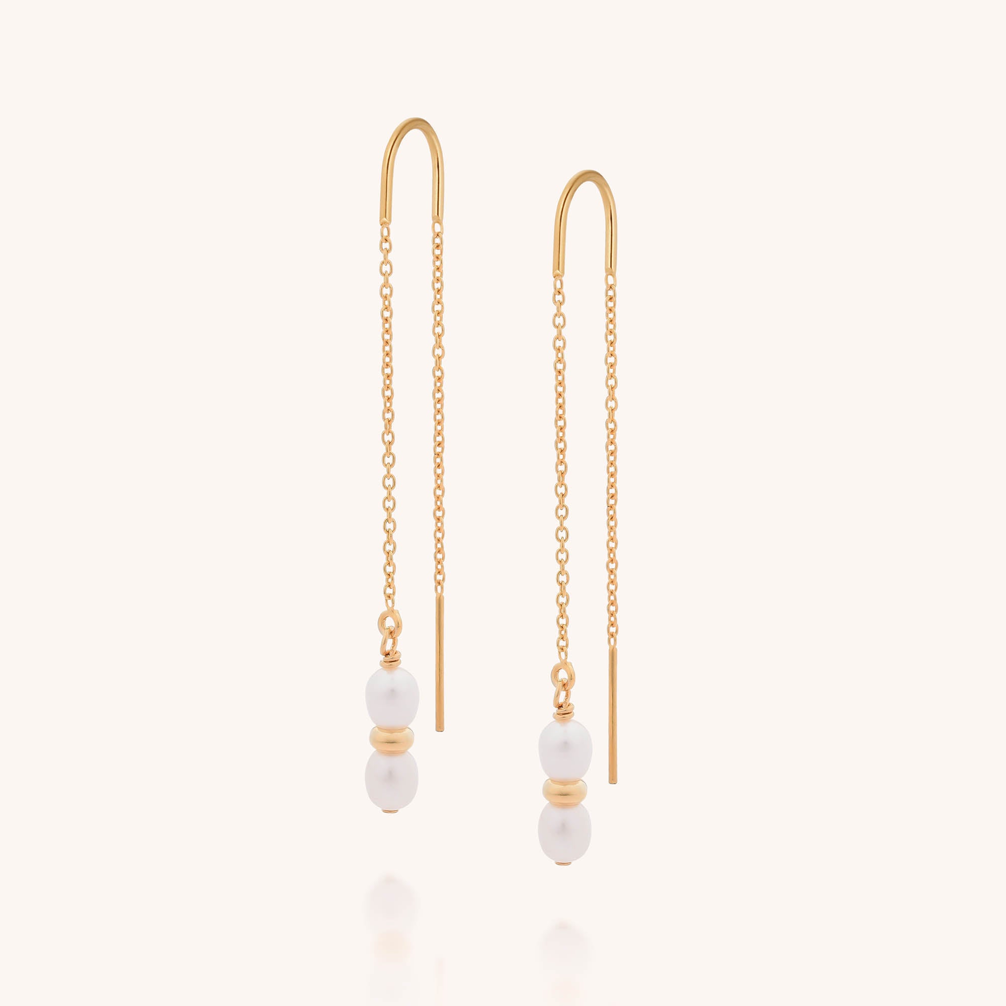 The Ellen Pearl Fall Earrings are gold threader earrings with a delicate chain, featuring two small freshwater pearls separated by a gold bead at the end. Photographed against a plain, light background.