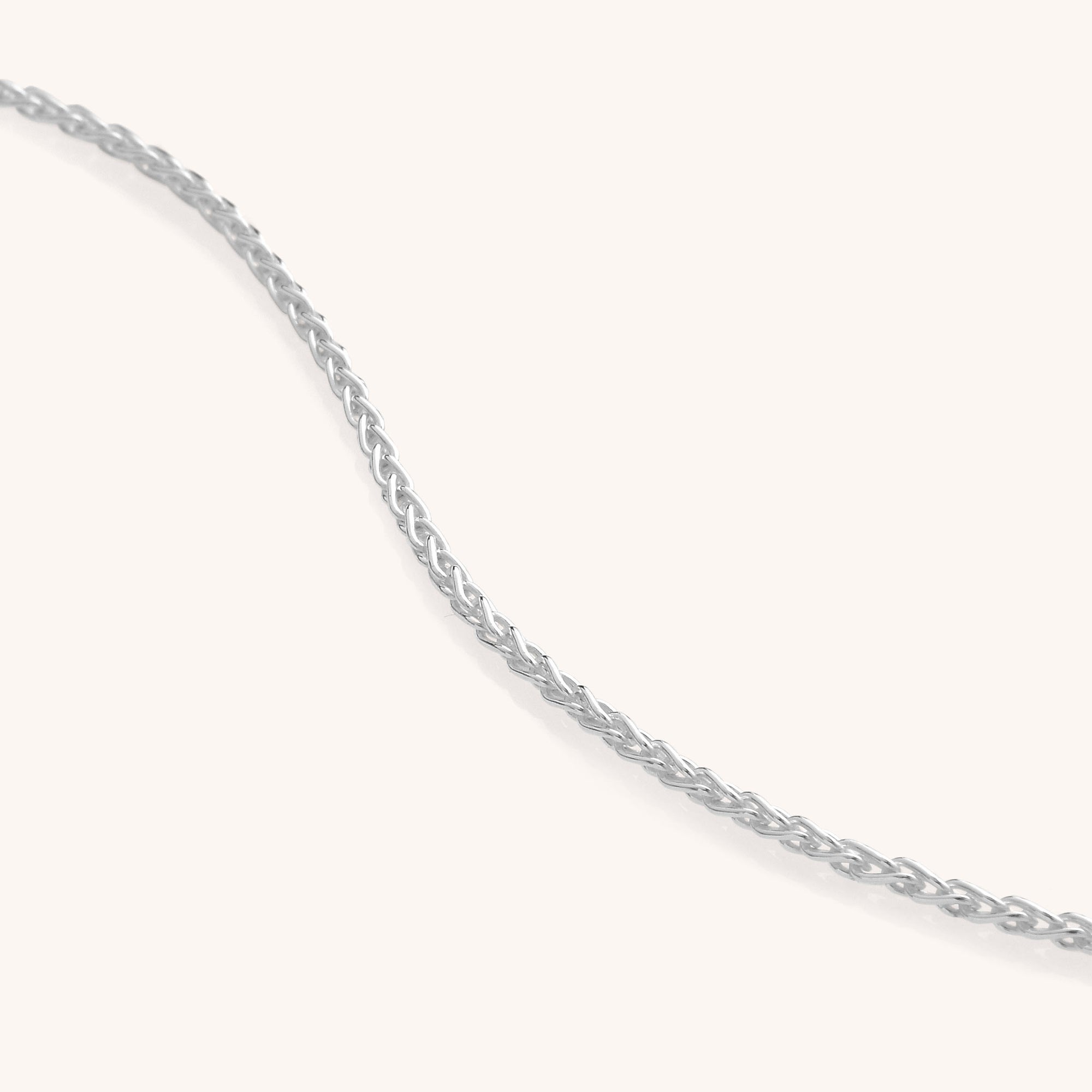 A close-up of a delicate Wheat Chain necklace in Eco Sterling Silver, displayed on a plain light background, with the chain gently curving across the image.