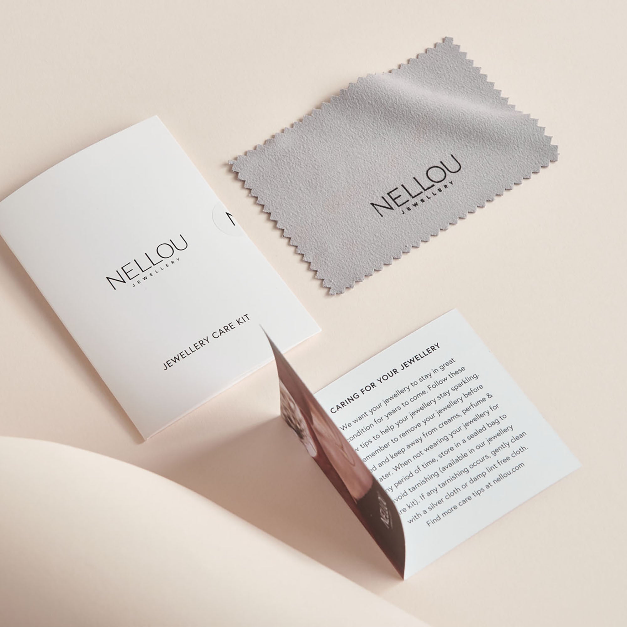Our Luxury Gift Wrapping includes a grey cleaning cloth, folded instruction card, and care booklet—all NELLOU branded—displayed on light beige. Perfect for jewellery lovers and pairs beautifully with our Nellou gift bag.