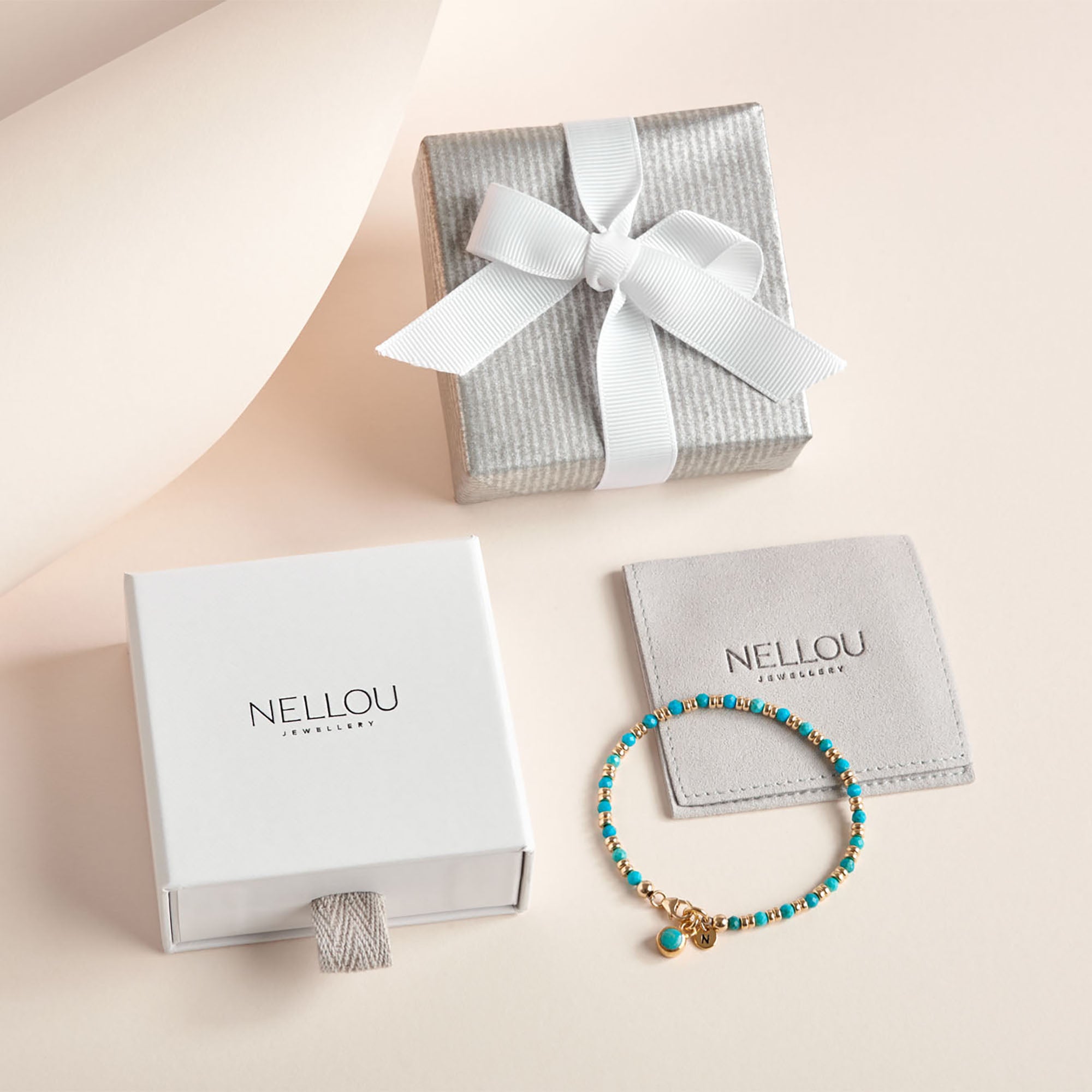 A turquoise and gold beaded bracelet is shown with Luxury Gift Wrapping, which includes a white Nellou Jewelry box, gray gift box with white ribbon, gray Nellou pouch, and elegant Nellou gift bag on a light beige background.