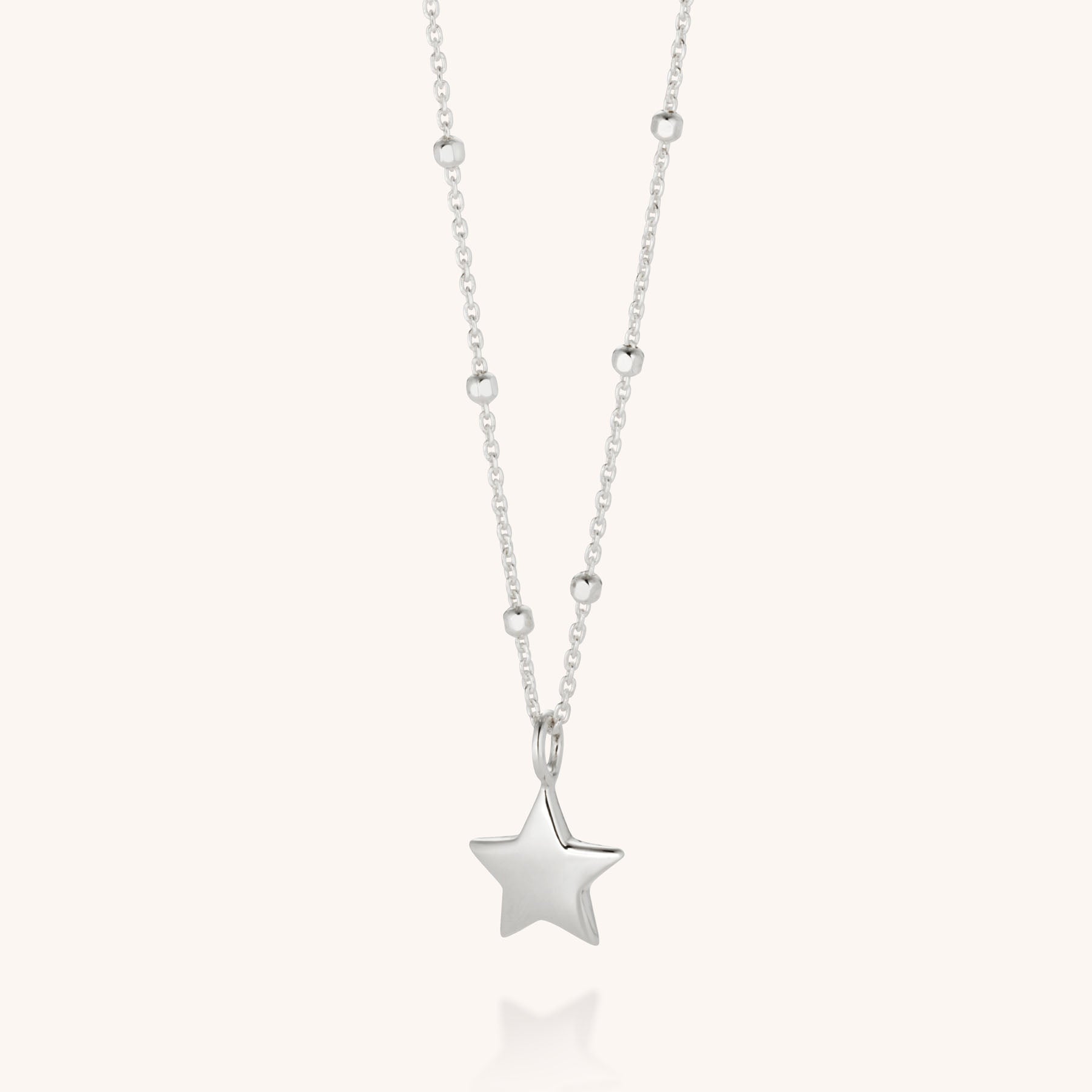 The Star Charm Necklace, an eco-friendly piece from our celestial-inspired collection, features a polished silver star pendant on a beaded chain with round accents, showcased on a light neutral background.