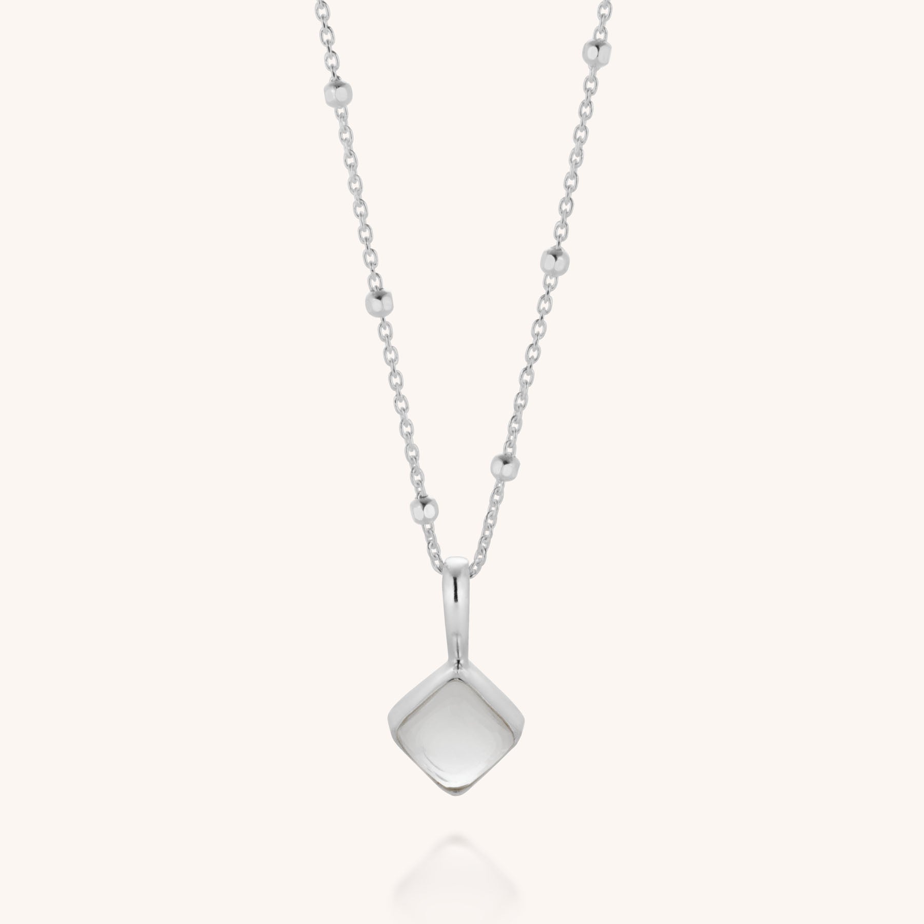 The Diamond April Birthstone Necklace is a delicate silver piece featuring a beaded chain and a small geometric square pendant with rounded edges, set with a natural crystal, displayed on a plain white background.