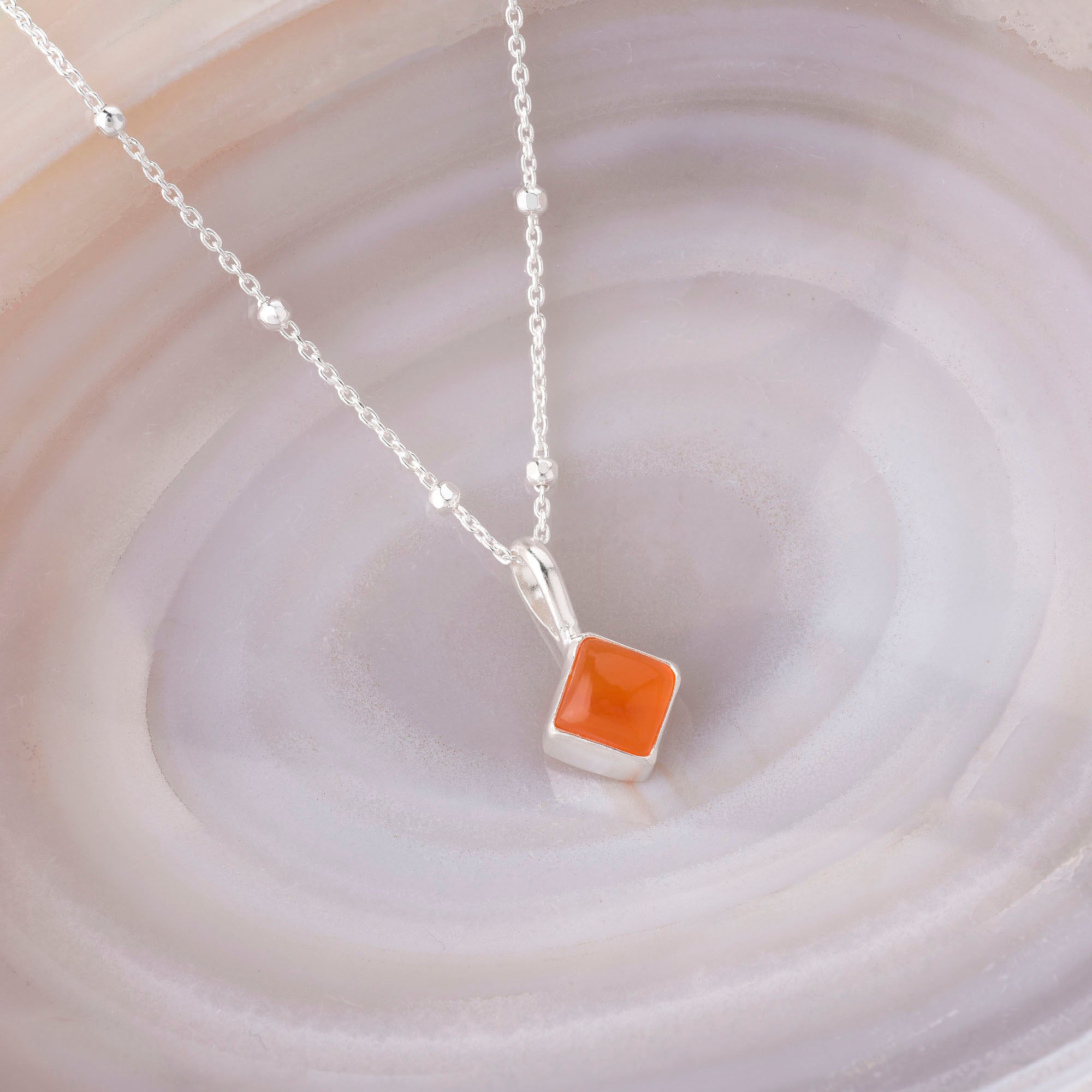 The Diamond Birthstone Necklace July, crafted in sterling silver with a square gemstone pendant, is showcased on a pink and white marbled surface.