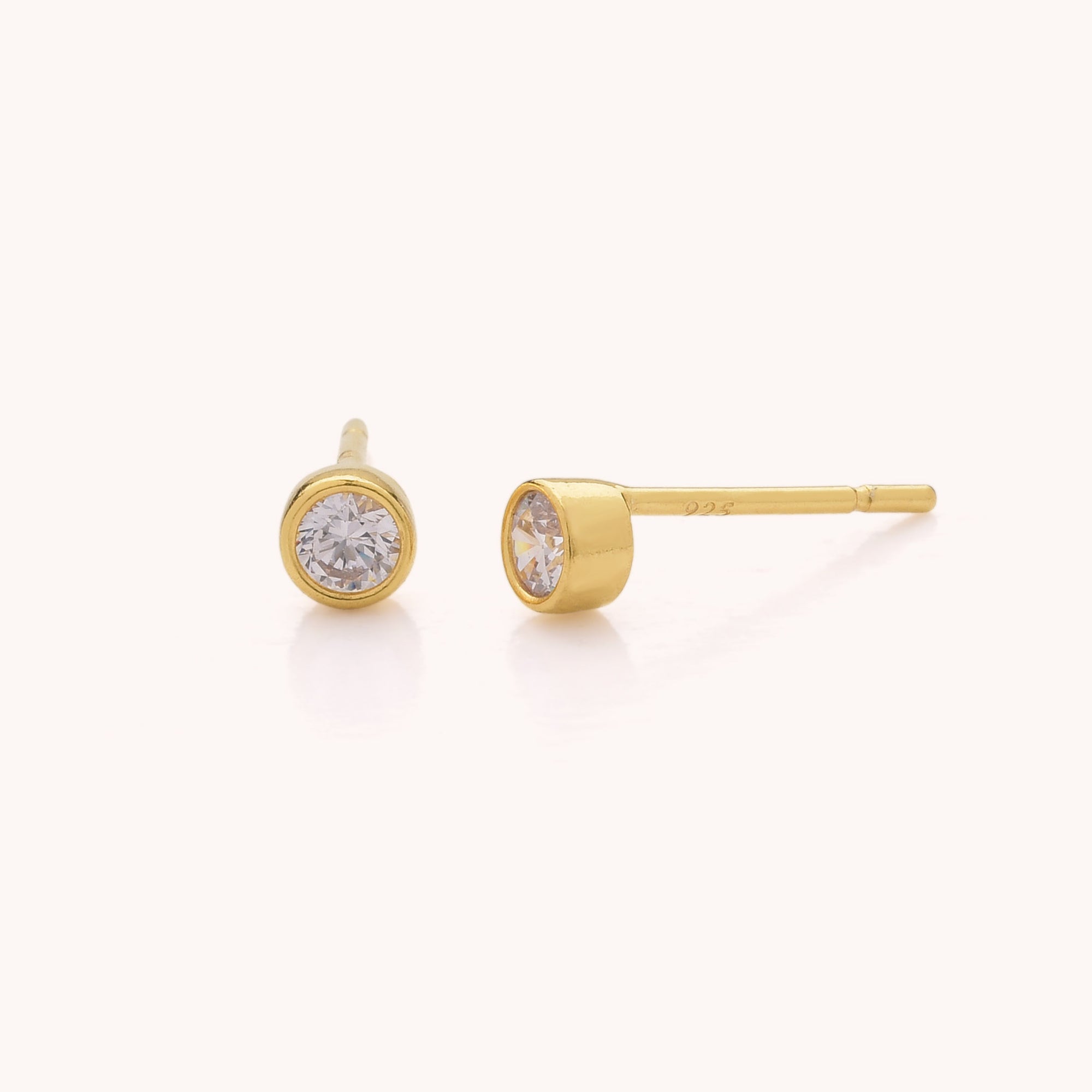 Dot Stud Earrings: a pair of gold stud earrings featuring round clear Cubic Zirconia stones in bezel settings, displayed on a plain light background.