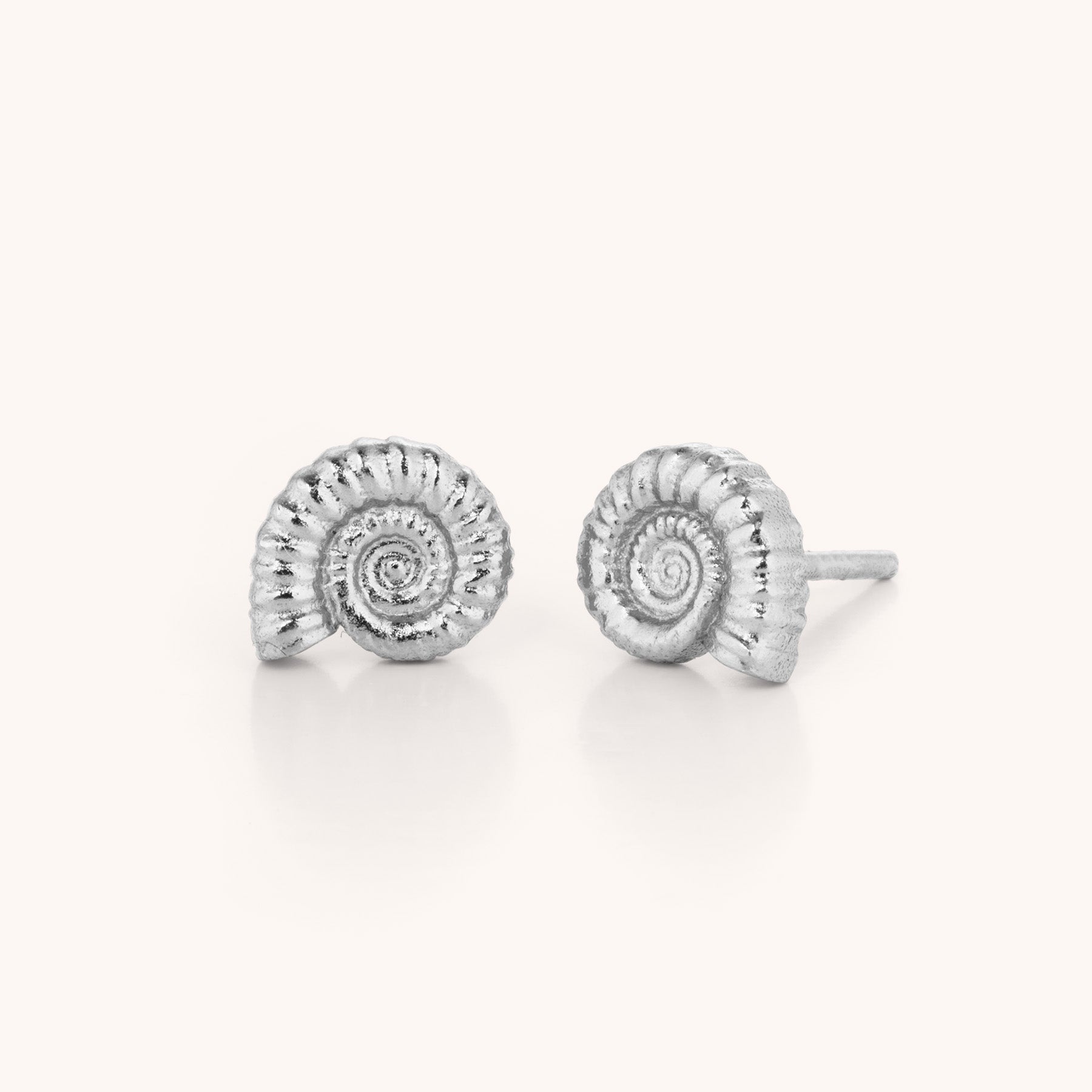 Ammonite Earrings: Silver stud earrings inspired by coiled fossil shapes, featuring detailed spirals and textured surfaces—an elegant, unique jewellery gift displayed on a simple light background.