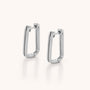 The Double Oblong Hoop Earrings feature a minimalist, modern silver design with a subtle double effect, displayed on a light neutral background.