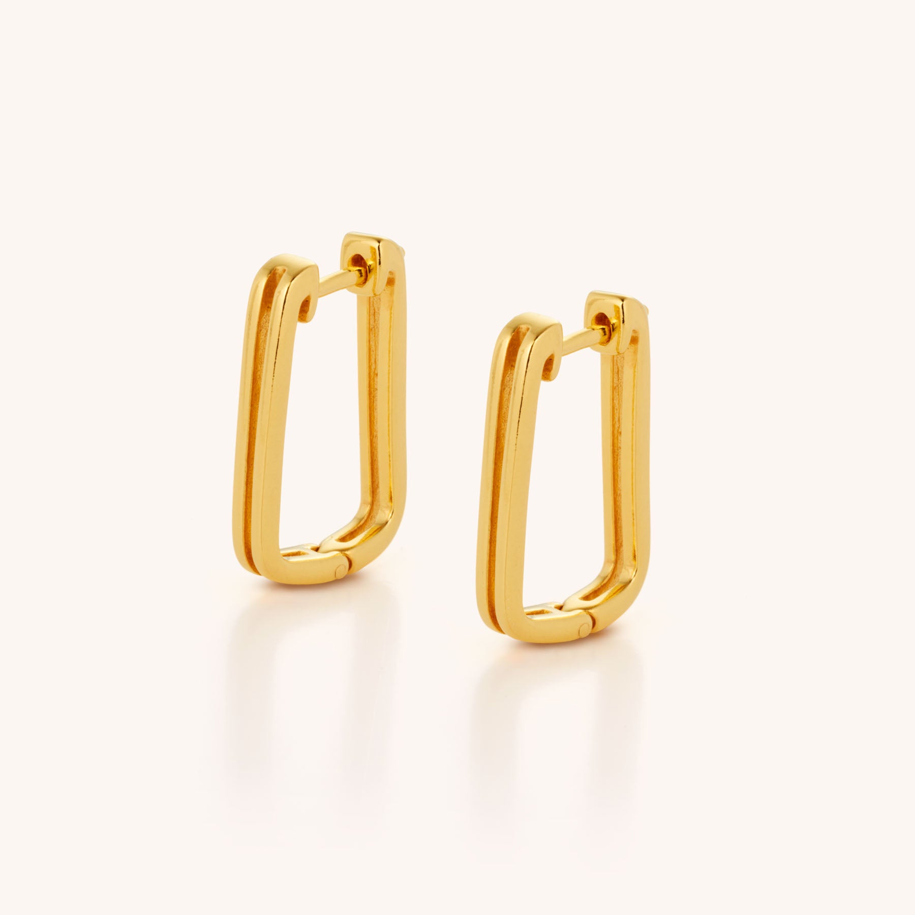 A pair of Double Oblong Hoop Earrings in gold with a rectangular, slightly curved shape and double effect design, displayed upright against a plain light background.