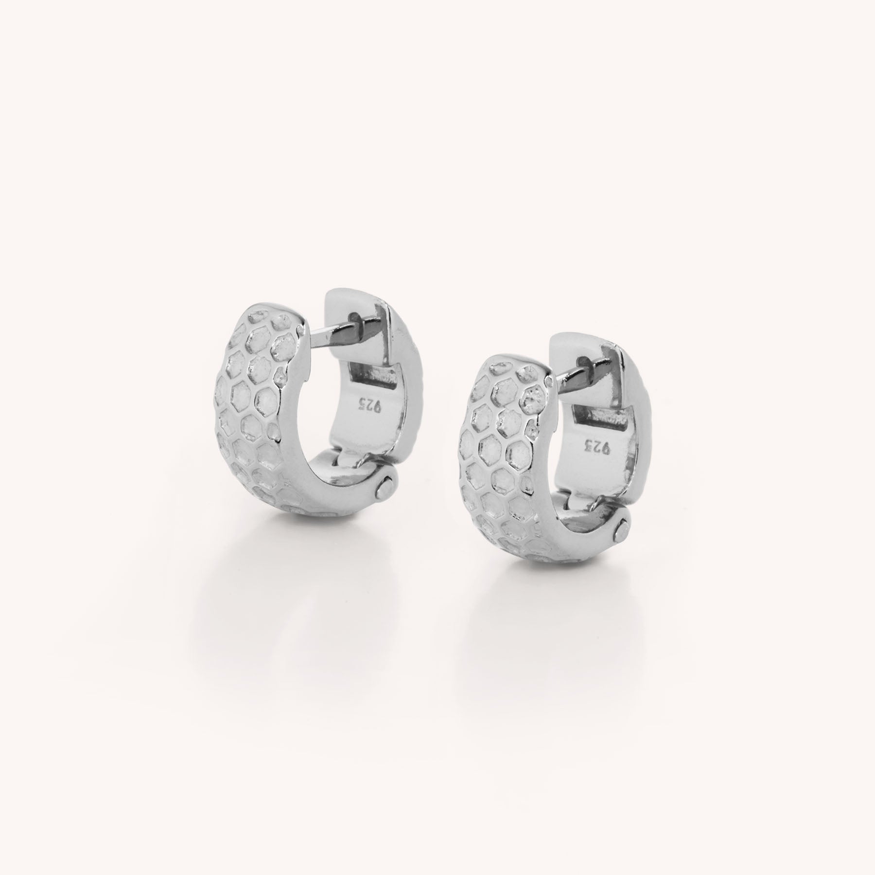 The Honeycomb Huggie Earrings are sterling silver ear hoops featuring a textured, honeycomb-like pattern on the outer surface, shown against a plain white background.