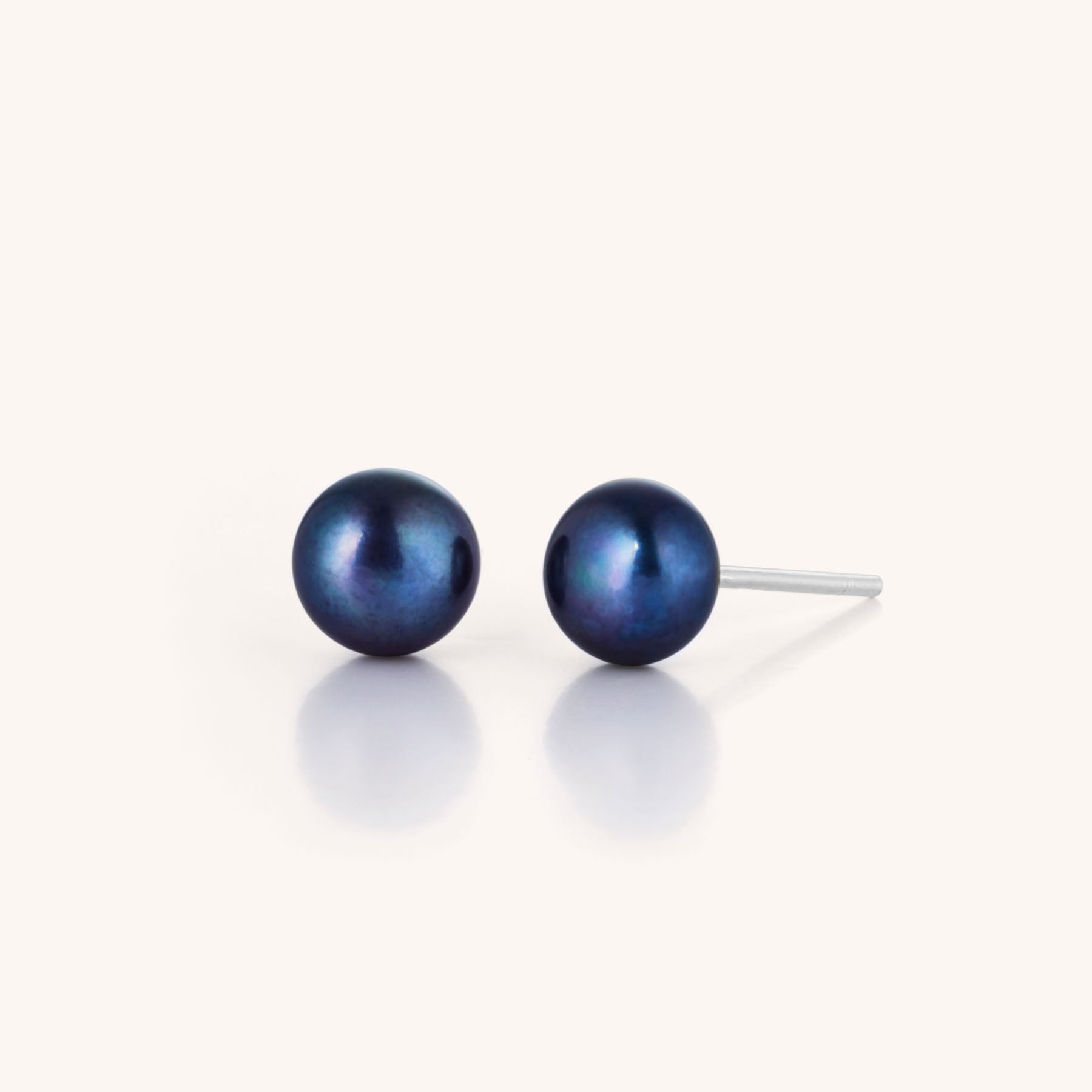 The Pearl Button Stud Earrings feature round black pearls on silver posts, displayed against a white background—ideal for adding timeless elegance to any outfit.