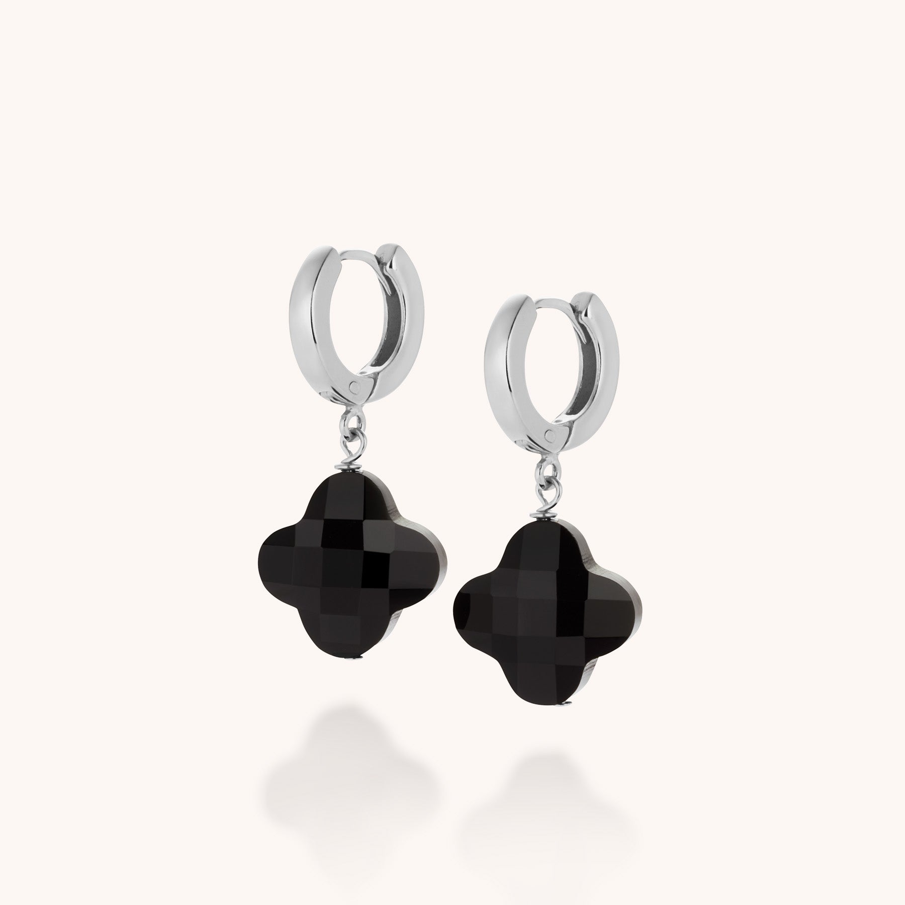 The Clover Gem Hoop Earrings feature sterling silver hoops with black faceted quatrefoil clover gemstone pendants, shown against a plain light background.