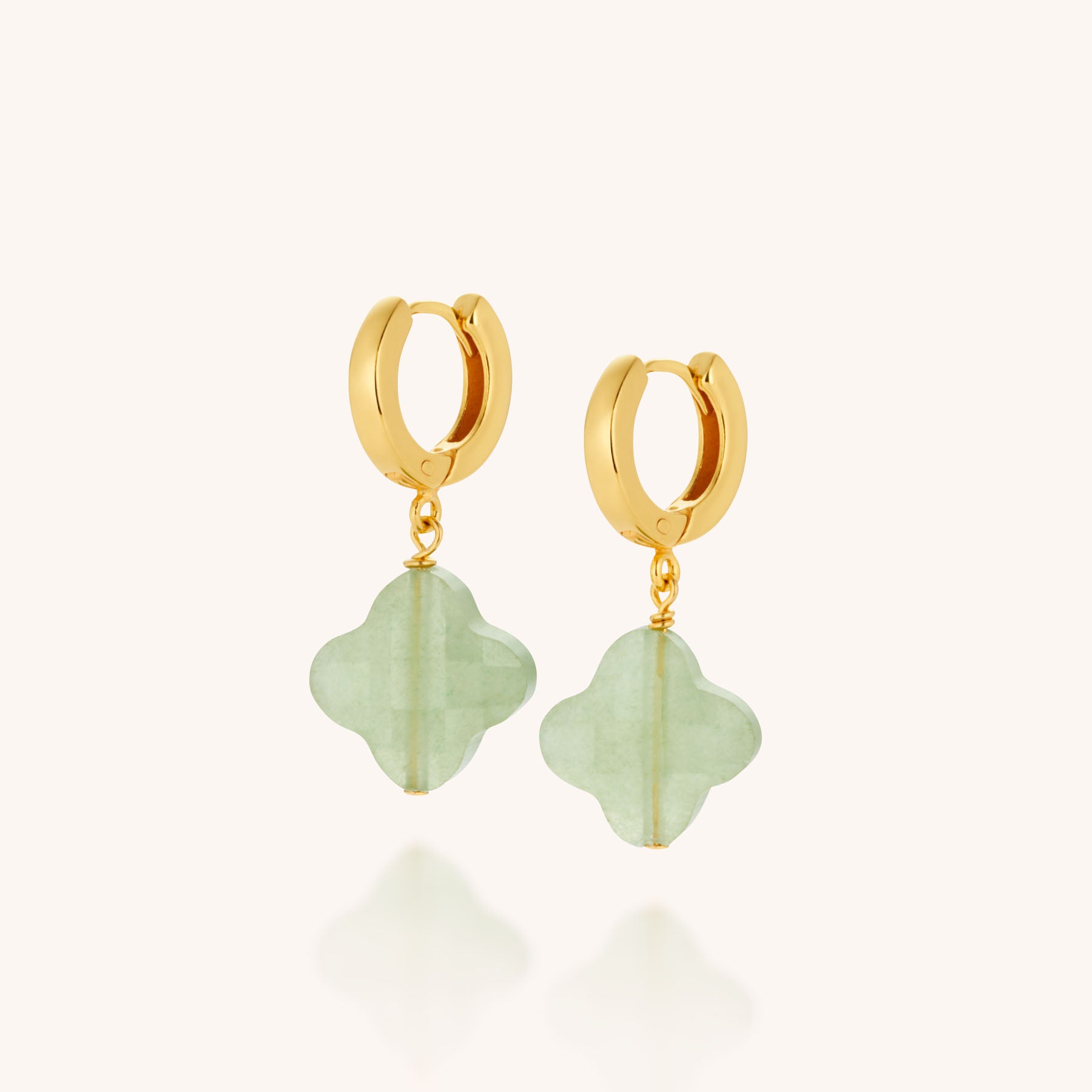 The Clover Gem Hoop Earrings feature a gold hoop design with dangling mint-green four-leaf clover charms and subtle gemstone accents, set against a light background.