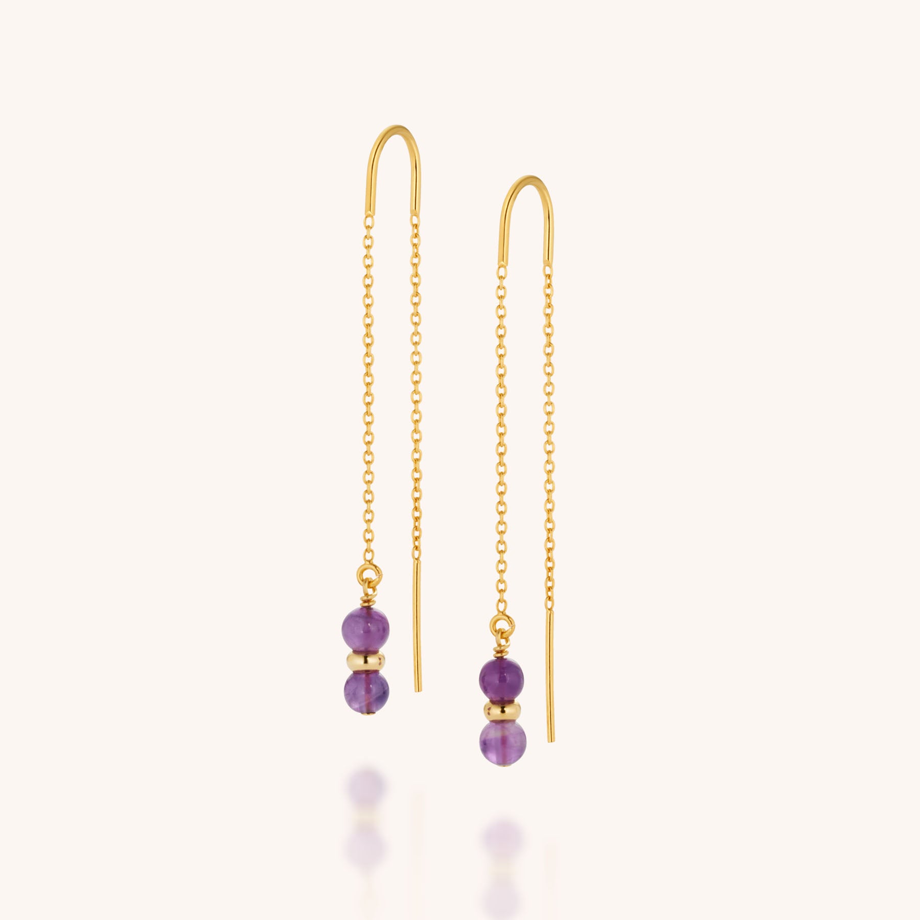The Fall Earrings Birthstone February are gold threader earrings with delicate chains, each adorned with two small round amethyst beads—the February birthstone—and a gold spacer bead at the ends, shown on a light background.