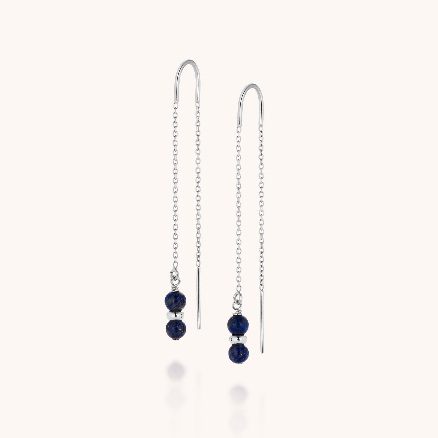 Showcased on a light background, the Fall Earrings Birthstone September feature delicate silver threader chains, each adorned with two small round denim blue beads and a silver bead at the end.