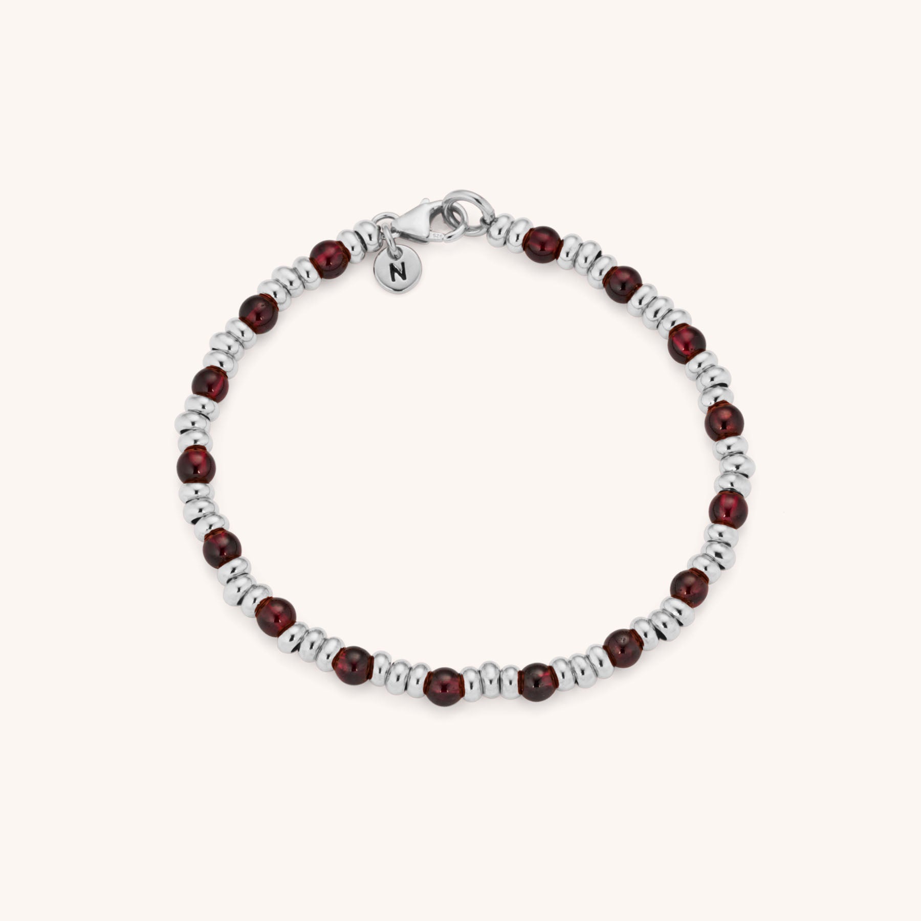 The Gem Bracelet January Birthstone features alternating silver and garnet beads, accented with a small silver charm engraved with the letter N near the clasp.