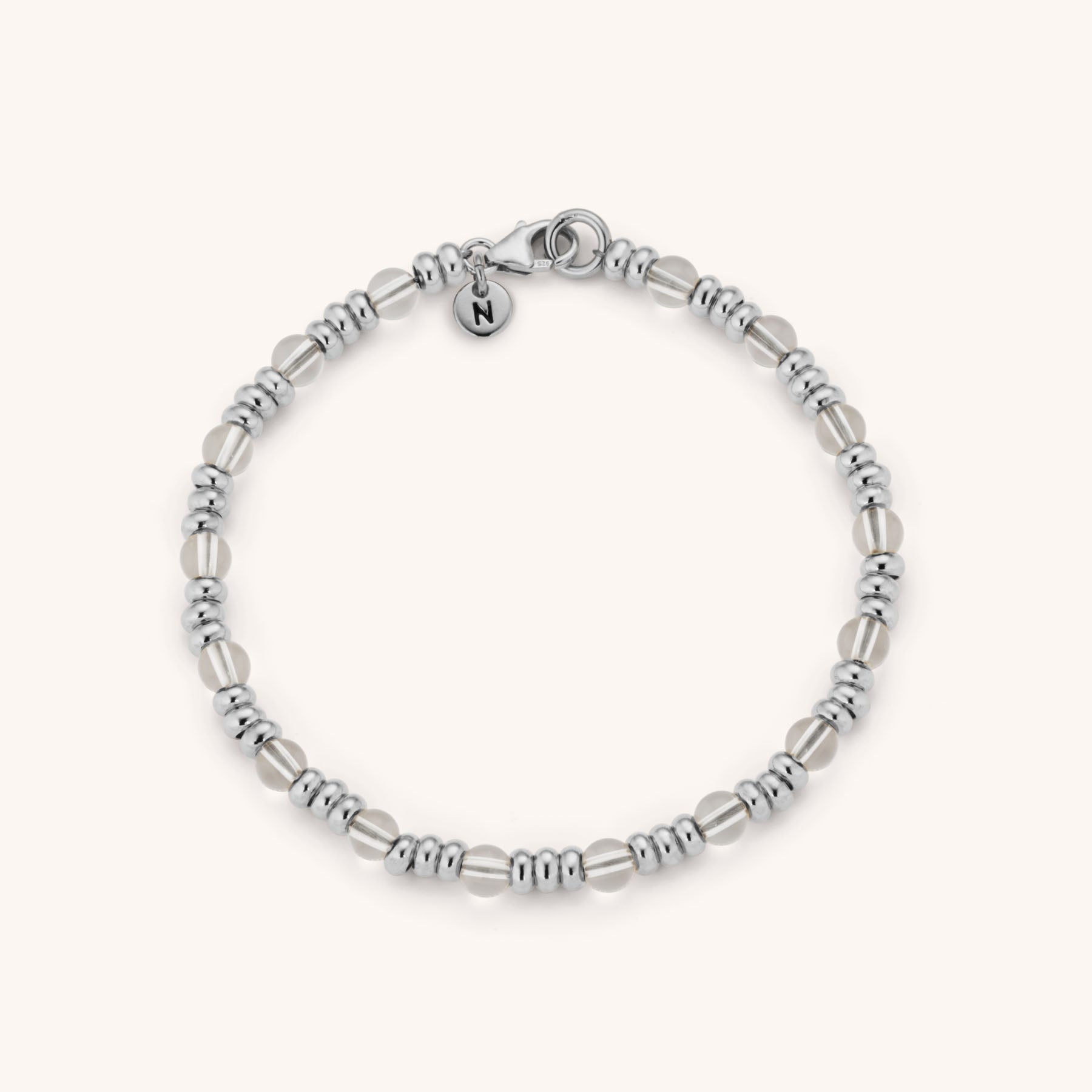 The Gem Bracelet April Birthstone features alternating eco-silver and translucent crystal beads, a round clasp, and a circular charm engraved with N, displayed on a light background.