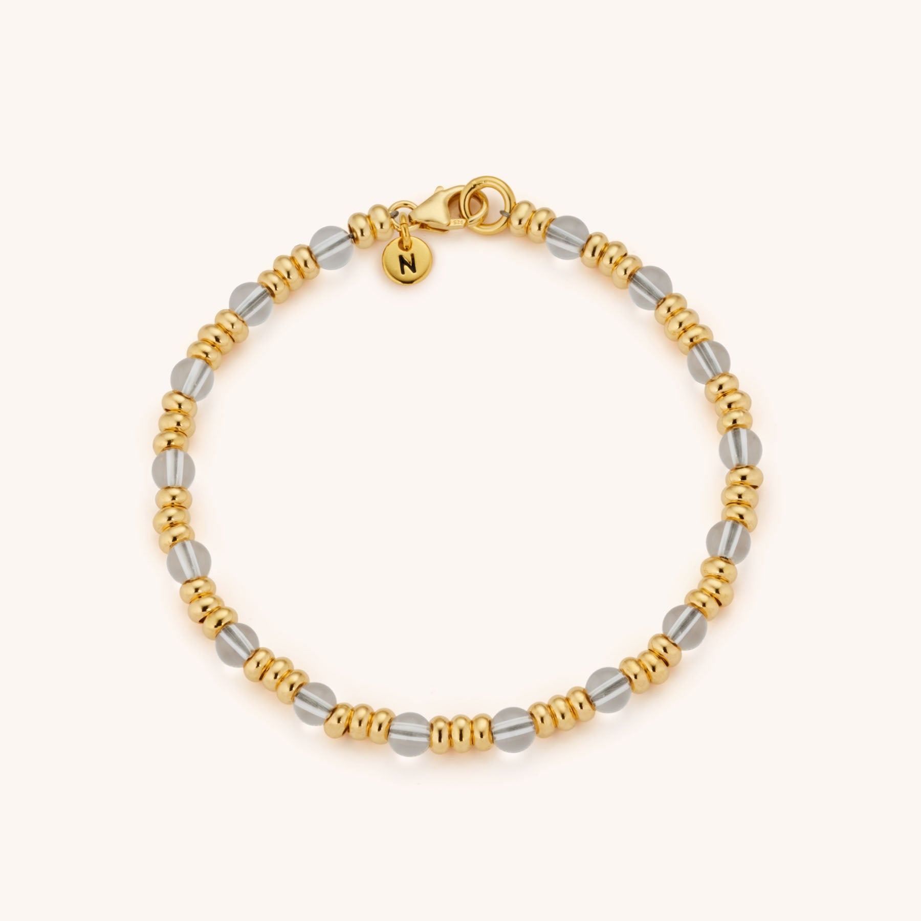 The Gem Bracelet April Birthstone features alternating gold and eco-silver beads, with a small gold charm engraved with the letter N near the clasp, displayed on a light background.