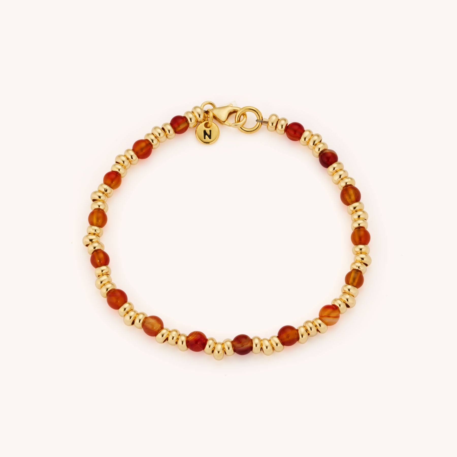 The Gem Bracelet July Birthstone features alternating round Carnelian beads—the July birthstone—with small gold beads, a gold clasp, and a charm engraved with the letter N.