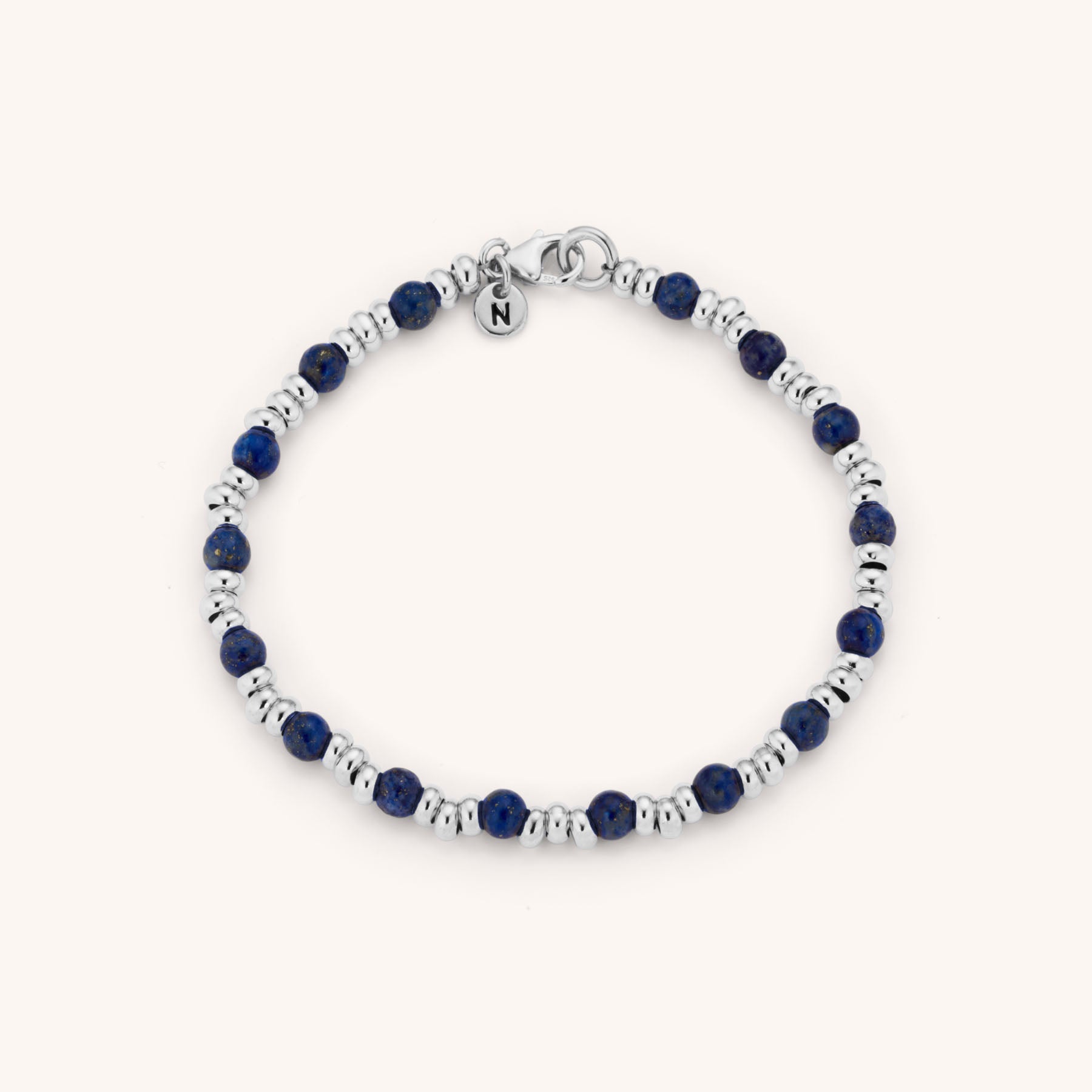 The Gem Bracelet September Birthstone showcases alternating small silver beads and round deep blue Lapis Lazuli stones, finished with a lobster clasp and a circular charm engraved with the letter “N.”.