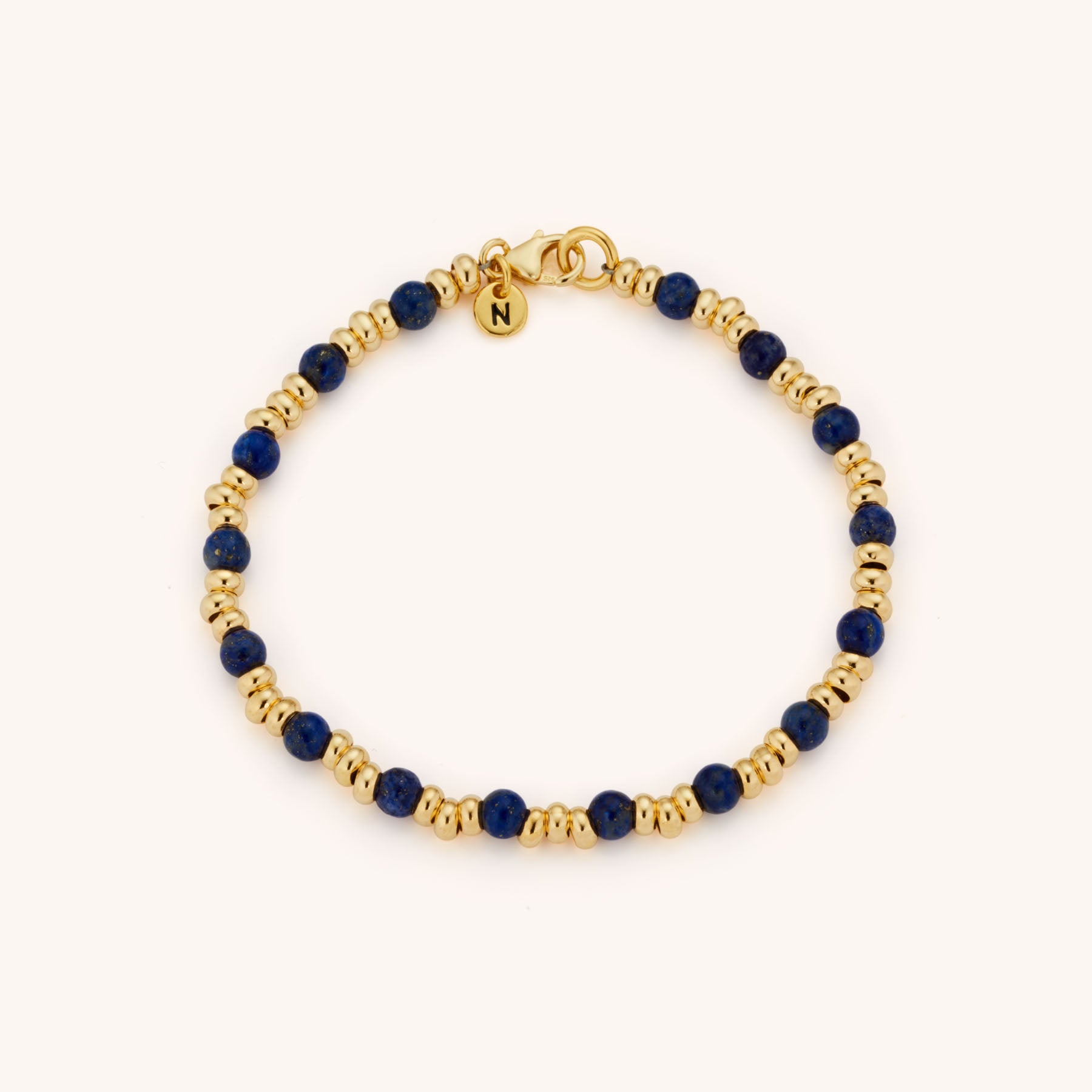 Gold and navy blue Gem Bracelet September Birthstone featuring Lapis Lazuli beads and a gold “N” charm, displayed on a plain light background.