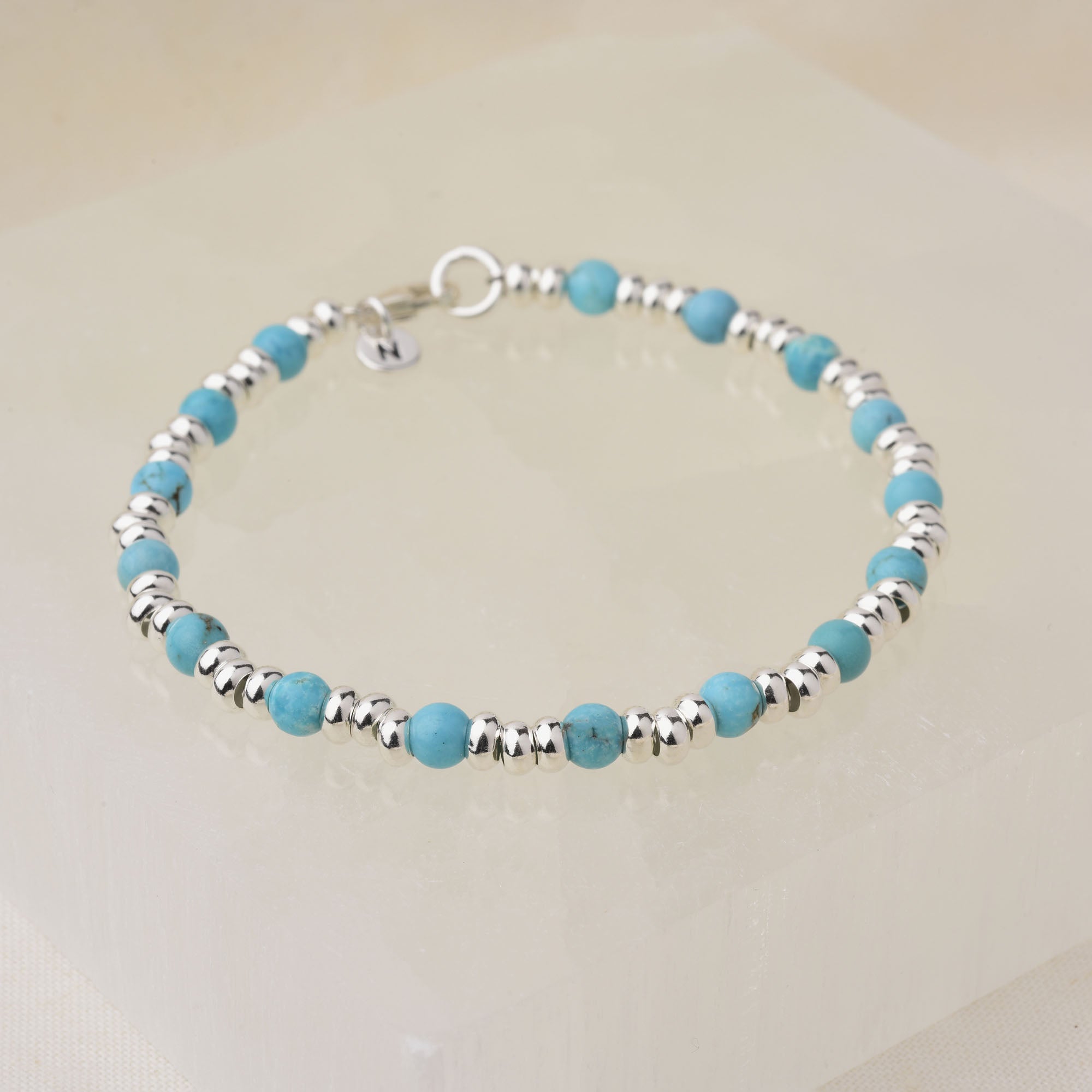 The Gem Bracelet December Birthstone features eco-silver beads and turquoise for December, finished with a silver clasp and round charm, displayed on a light translucent square.