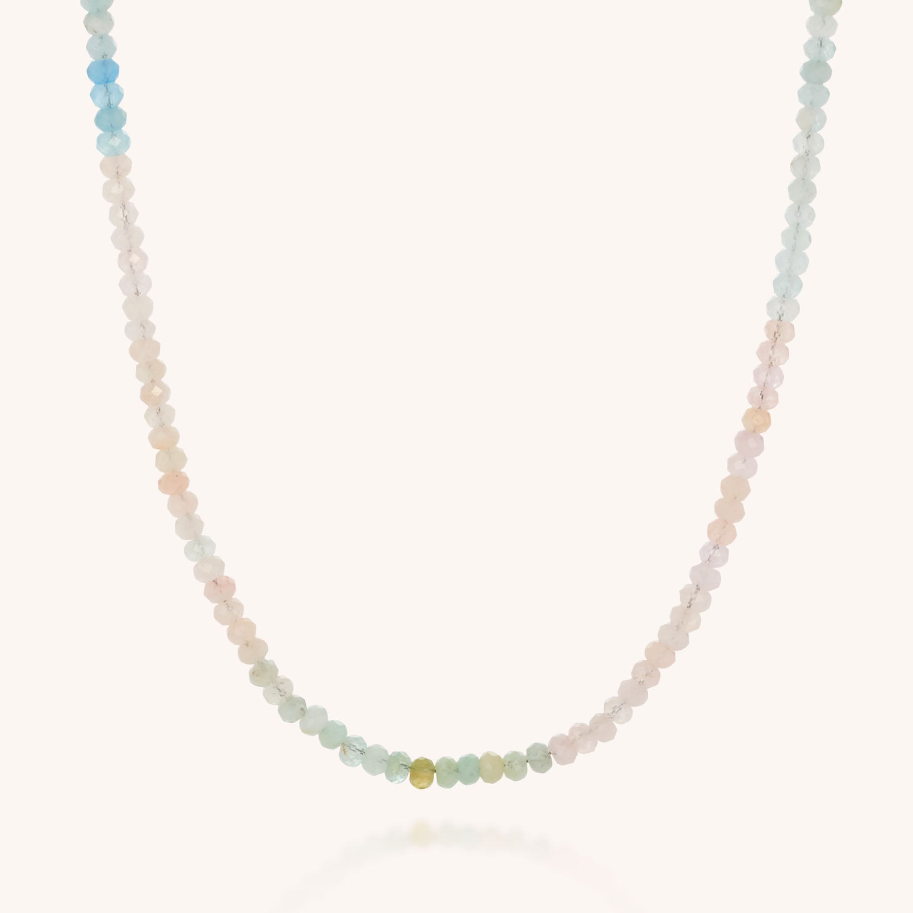 The Mini Bead Necklace showcases small, faceted pastel gemstones arranged in a gradient and finished with a sterling silver clasp, set against a simple light background.