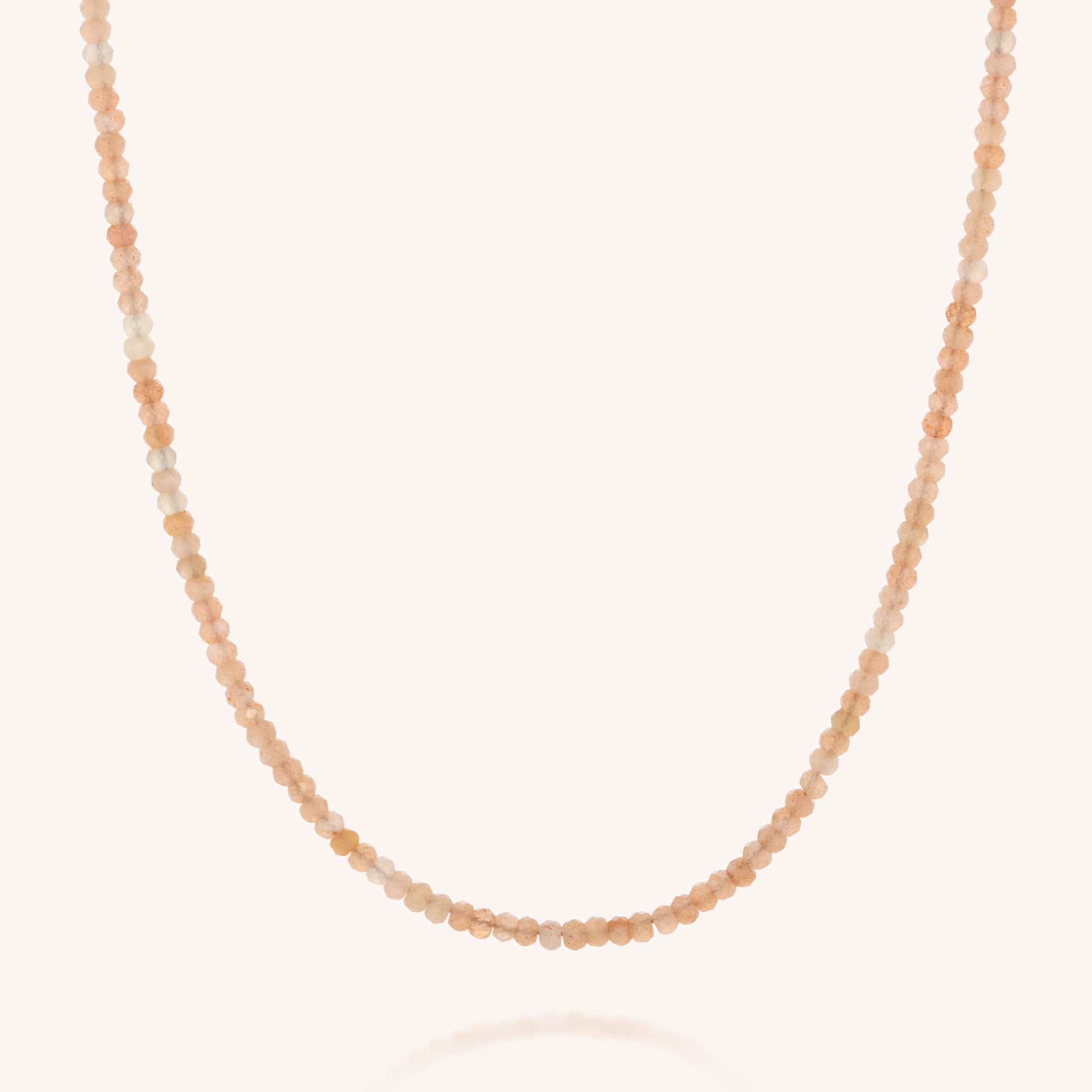 The Mini Bead Necklace features small, round faceted gemstone beads in soft peach, blush, and cream tones, arranged on a single strand with a sterling silver clasp. Photographed against a plain white background.