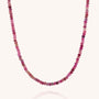 The Mini Bead Necklace features small, faceted round gemstone beads in pink and red shades, evenly strung on a thin, nearly invisible cord with a sterling silver clasp.