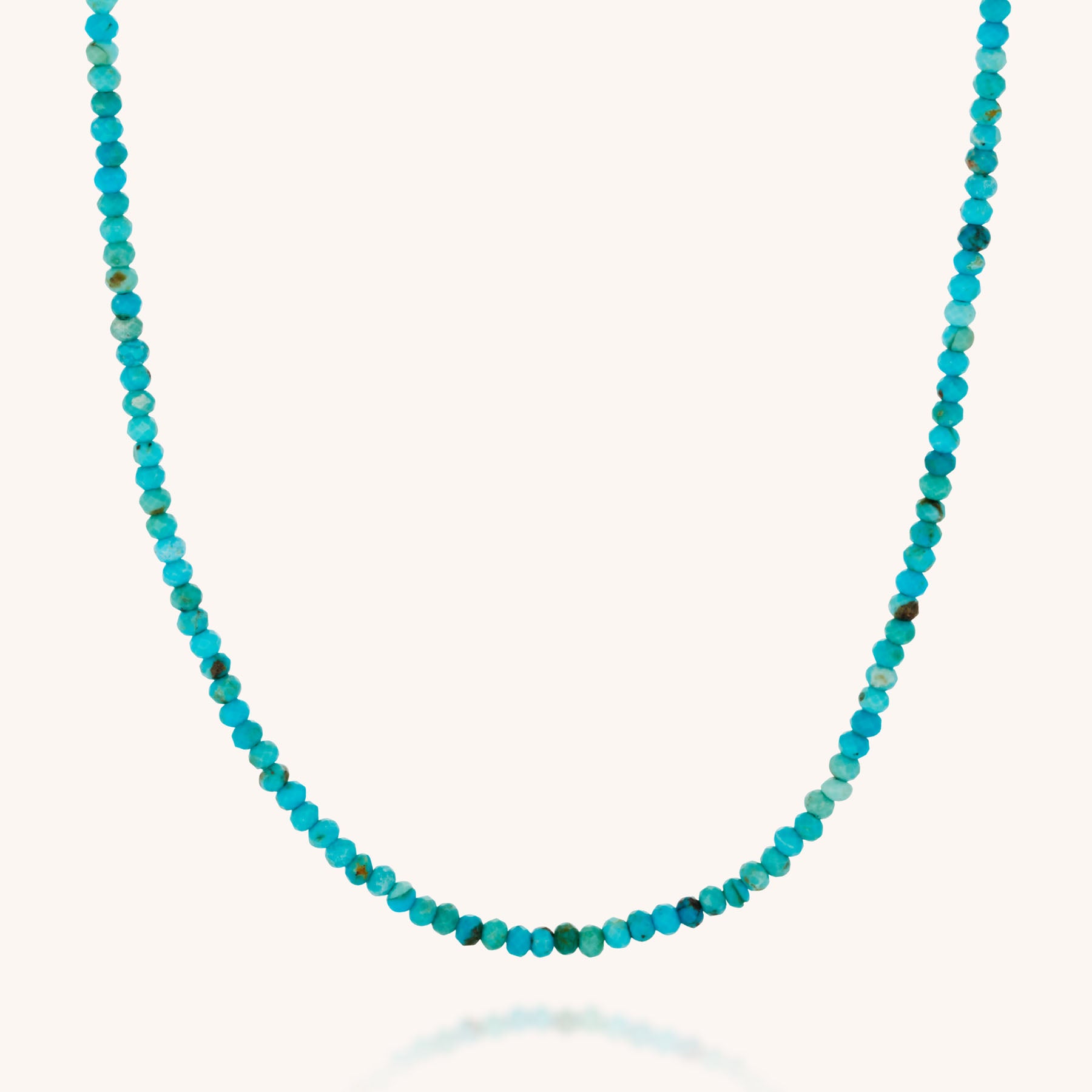 The Mini Bead Necklace features small, round turquoise gemstones evenly strung together with a sterling silver clasp, creating a simple and elegant loop displayed against a plain white background.