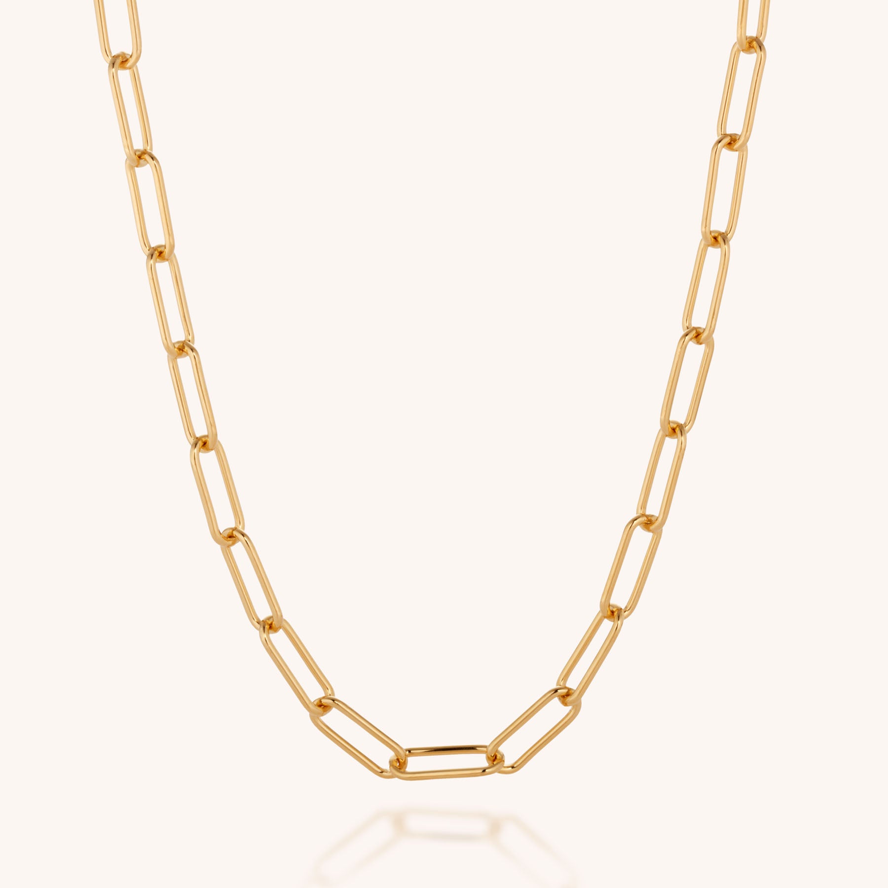 The Paperclip Necklace features elongated oval links and is shown on a light background, forming a curved shape that emphasizes its modern, simple, and elegant design.