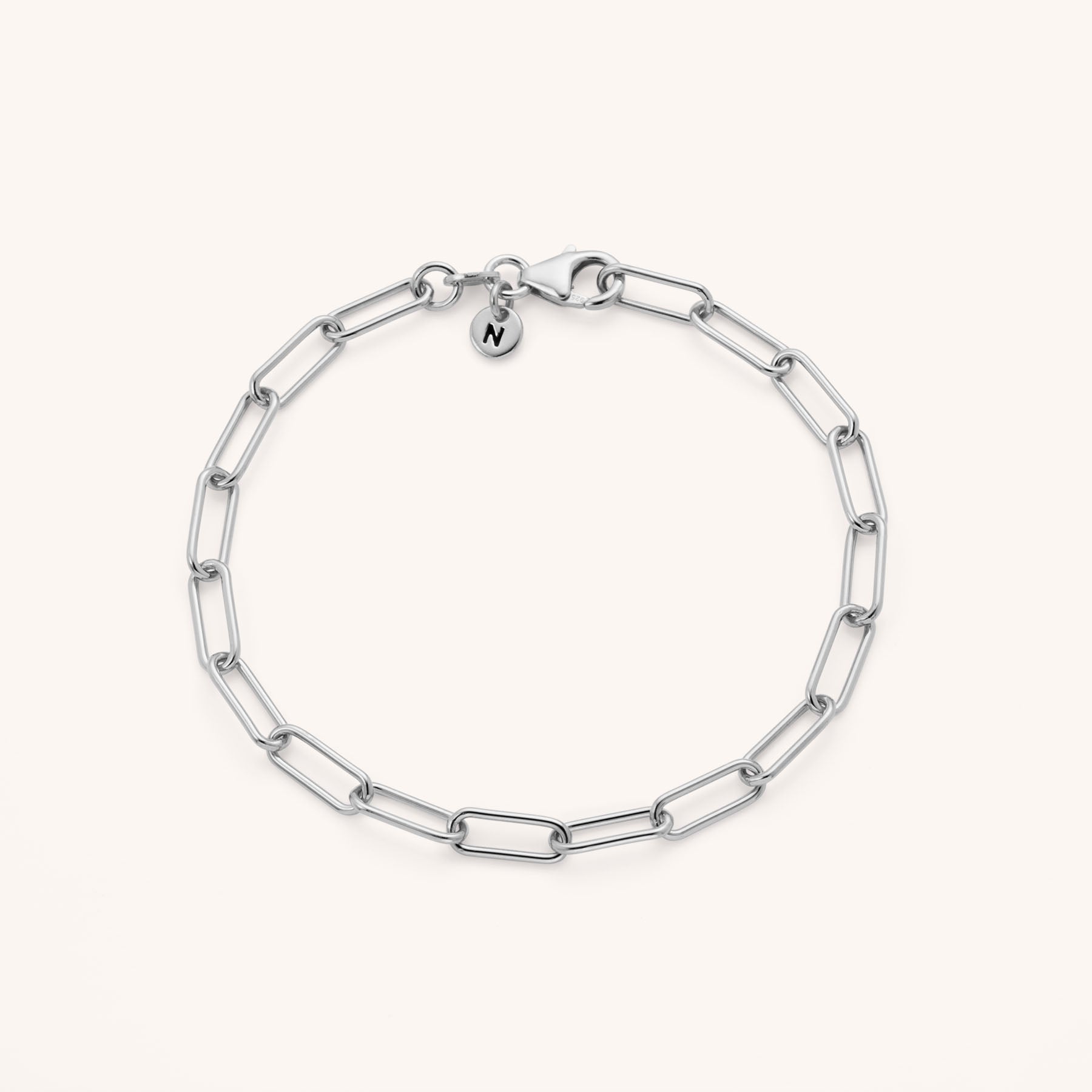 The Paperclip Bracelet is crafted from eco silver with elongated links, a lobster clasp, and a round charm engraved with N. Adjustable for the perfect fit, it’s displayed on a plain light background.
