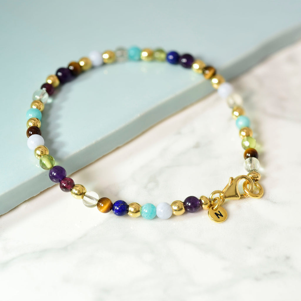 Multi gemstone bracelet in gold on an aqua tile