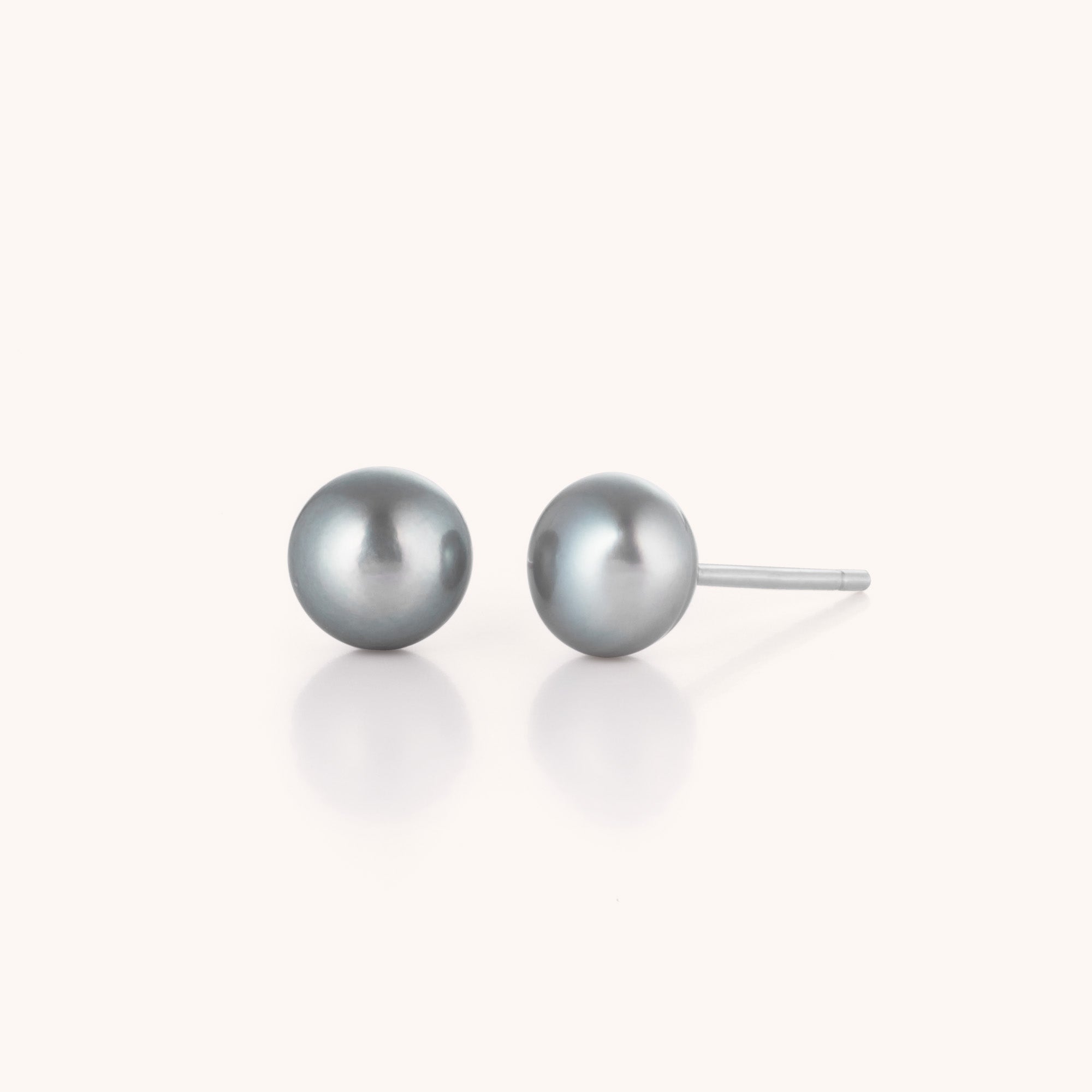 The Pearl Button Stud Earrings feature round, silver-grey pearls on simple posts, showcased against a light background—an ideal choice for timeless elegance with any classic outfit.