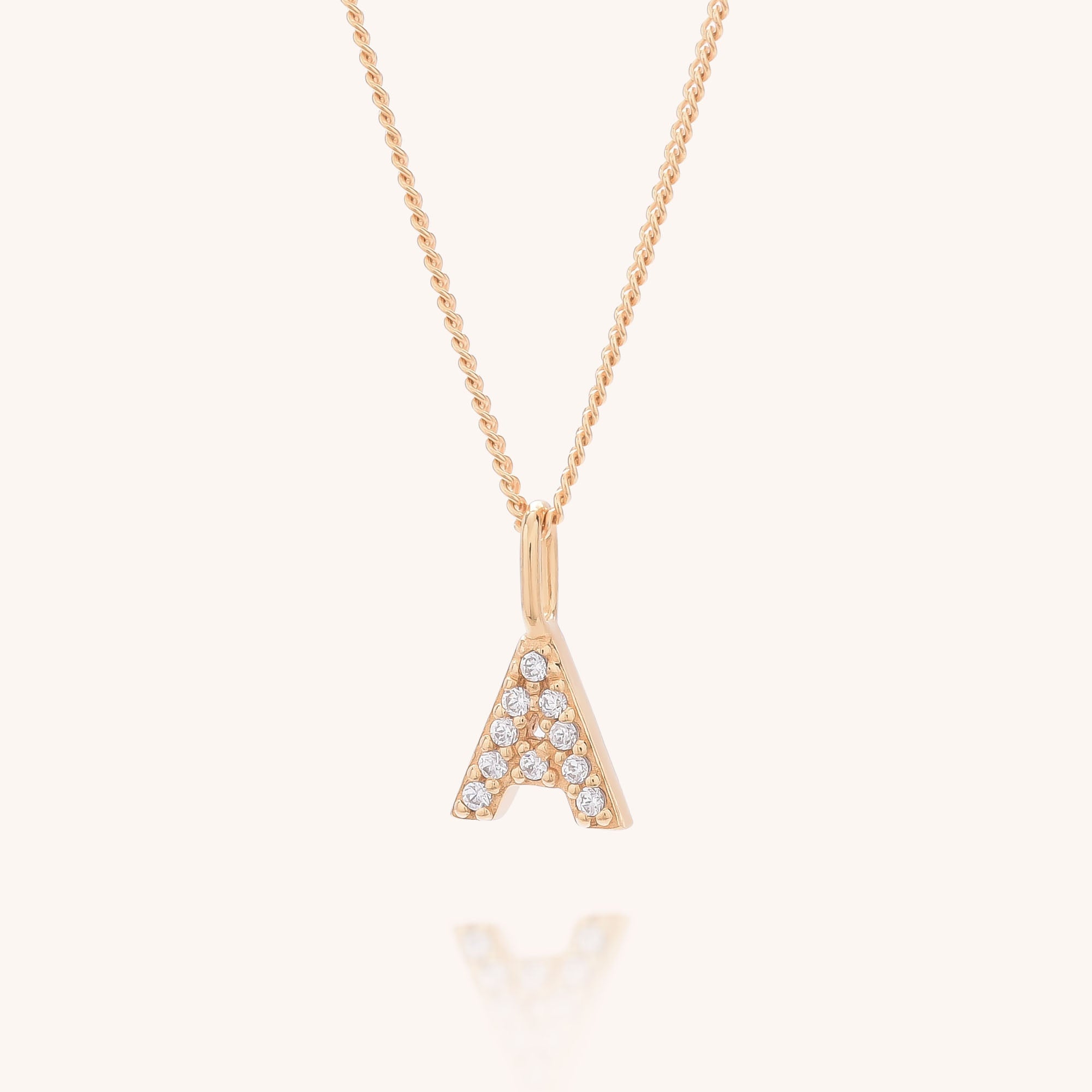 The Initial Sparkle Necklace features a gold A-shaped pendant adorned with round cubic zirconia stones, displayed against a plain light background.