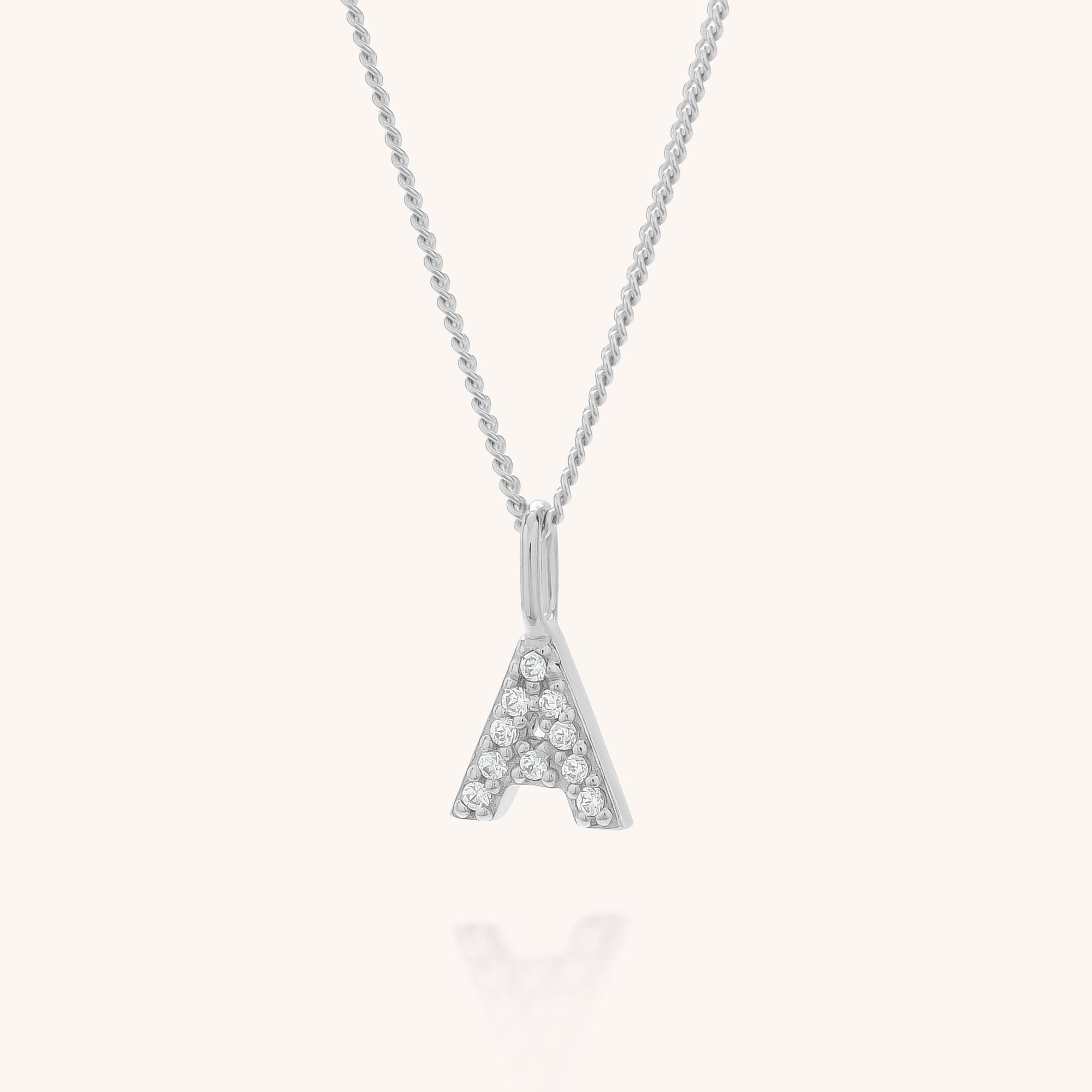 The Initial Sparkle Necklace features a silver pendant shaped like the letter A, adorned with sparkling cubic zirconia stones, and is presented on a simple light background.