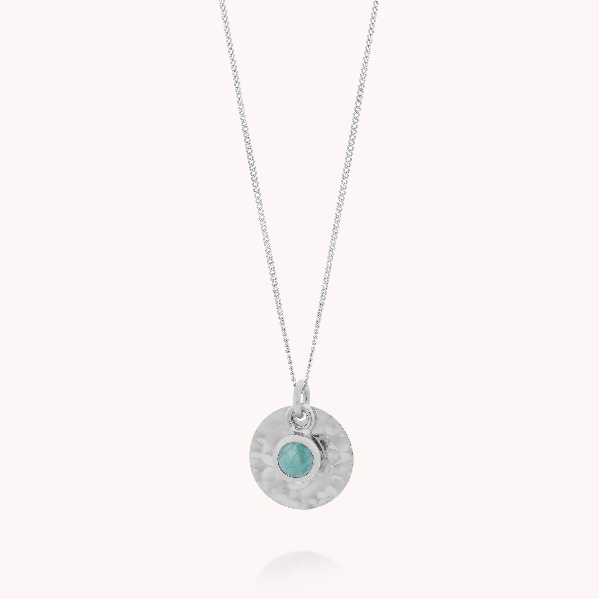 The Amazonite Luna Disc Necklace features a fine silver chain, a round hammered silver pendant, and a small amazonite gemstone at the center—ideal for fans of natural gemstone jewelry.