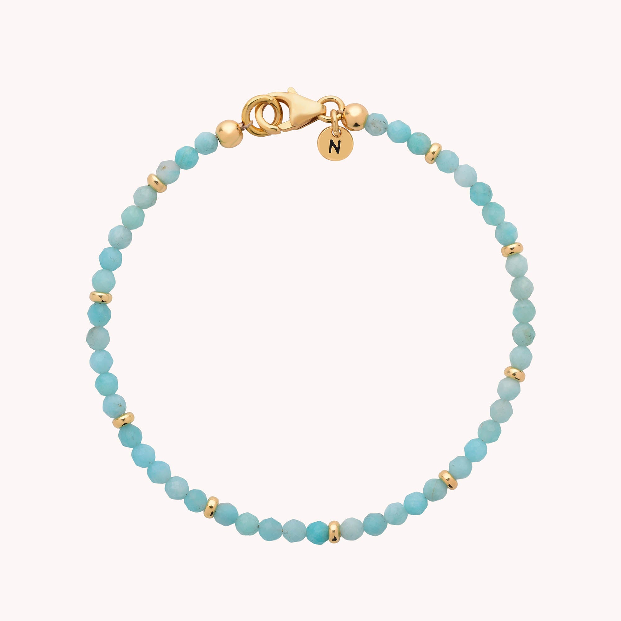 Introducing the Amazonite Orbit Bracelet—a delicate piece featuring small round amazonite beads accented with gold spacer beads. This elegant bracelet is crafted from gold plated eco sterling silver and is finished with a secure gold lobster clasp, plus a charming round gold charm engraved with the letter N for a personalized touch.