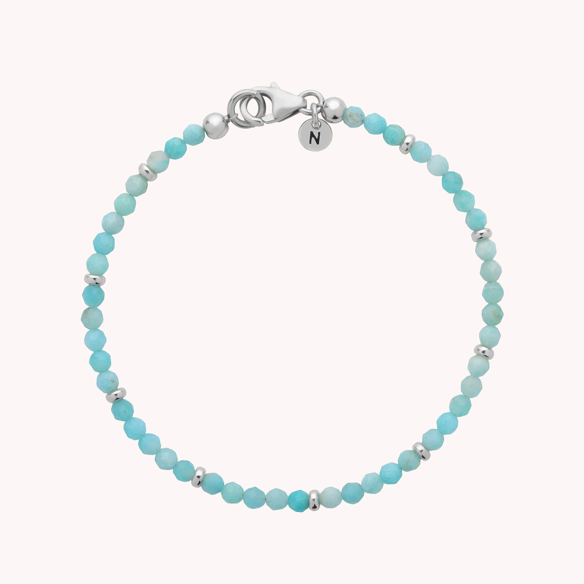 Introducing the Amazonite Orbit Bracelet—a delicate sterling silver piece adorned with small turquoise and shimmering amazonite beads, accented with silver spacer beads, a secure silver clasp, and finished with a round charm engraved with the letter N.