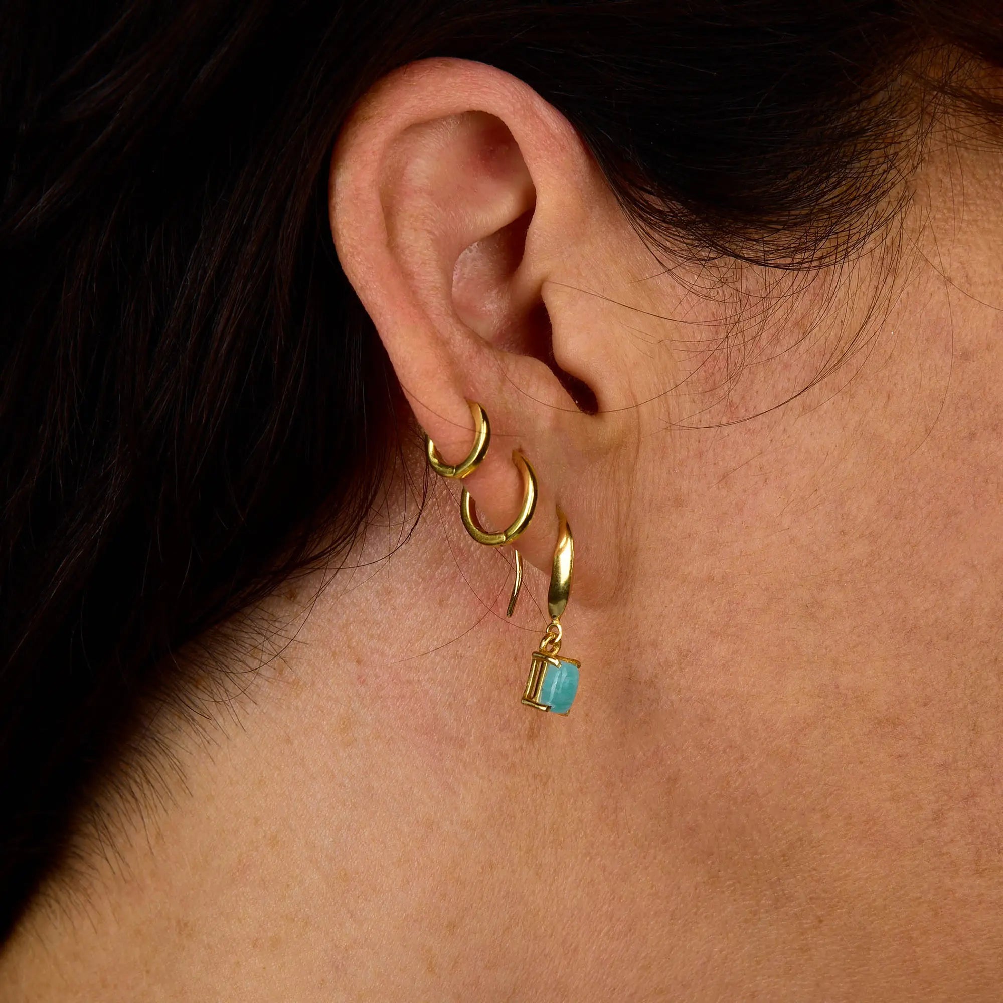 A close-up of a person’s ear wearing three gold hoop earrings, with the lowest hoop showcasing the Amazonite Octavia Drop Earring—featuring a small rectangular amazonite charm in an elegant octagonal setting.