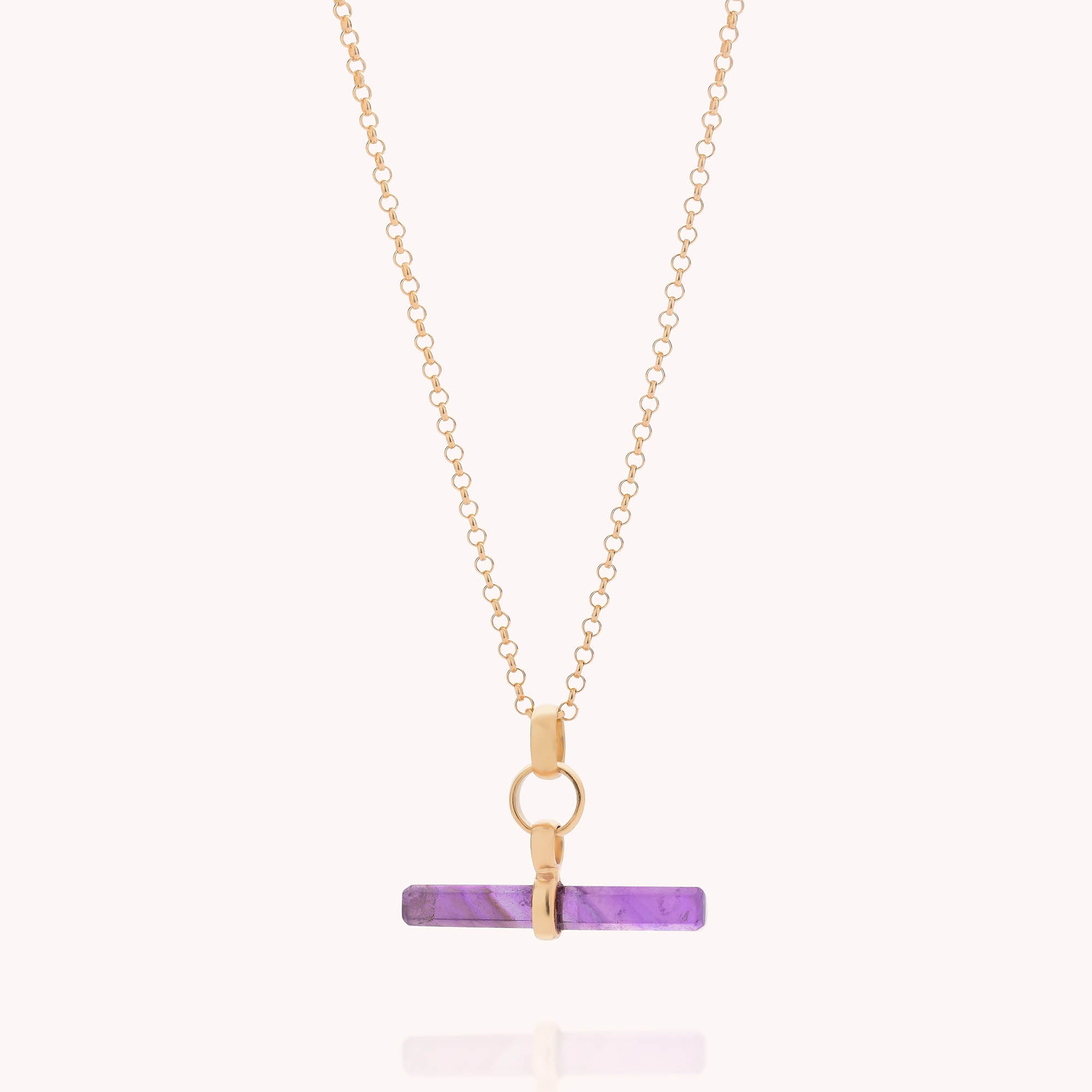 The Gemstone T Bar Necklace features a gold chain with a horizontal purple semi-precious stone bar pendant, secured by a gold circular clasp and link, displayed against a plain light background.
