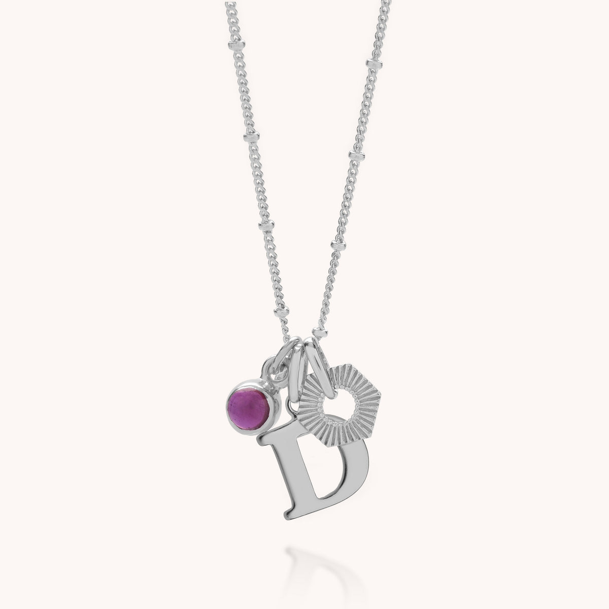 Introducing the HEX Personalised Birthstone Necklace – Sterling Silver: a delicate sterling silver necklace featuring three distinctive charms—a pink birthstone gemstone, a textured hexagon, and a bold letter D pendant. The fine chain is accented with subtle silver beads, making this personalized necklace the perfect way to elevate your style with a unique touch.