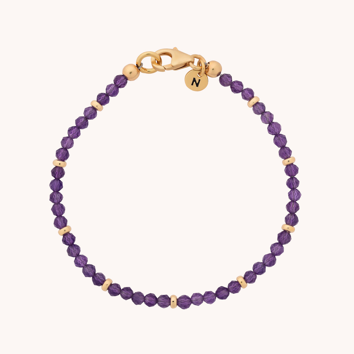 The Amethyst Orbit Bracelet – February features small purple amethyst beads and gold accents, finished with a gold clasp and a round gold charm engraved with the letter N—making it a perfect gift for anyone who cherishes the February birthstone.