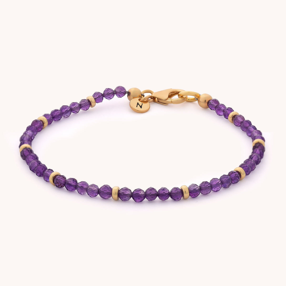 Introducing the Amethyst Orbit Bracelet - February: an elegant accessory adorned with small, round amethyst beads and gold spacers, finished with a gold clasp and a dainty gold charm engraved with the letter N—perfect for celebrating the February birthstone.