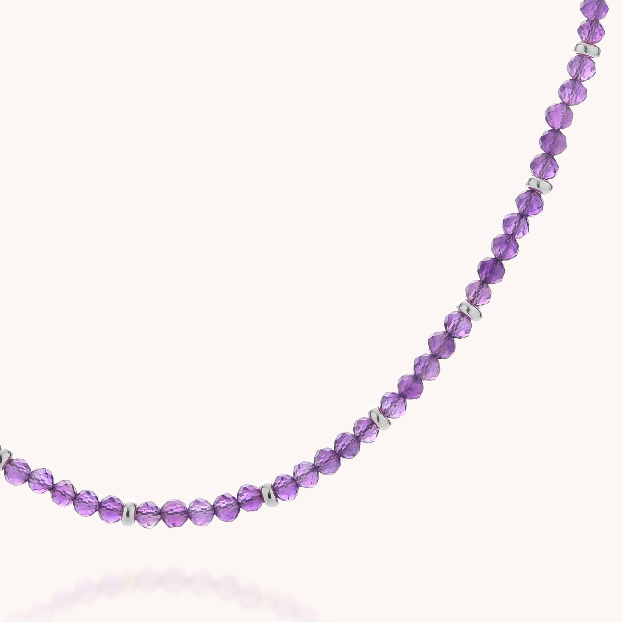 A close-up of the Amethyst February Birthstone Orbit Necklace, handcrafted with faceted purple amethyst beads—the February birthstone—each separated by delicate silver spacers and artfully arranged in a gentle curve on a light background.