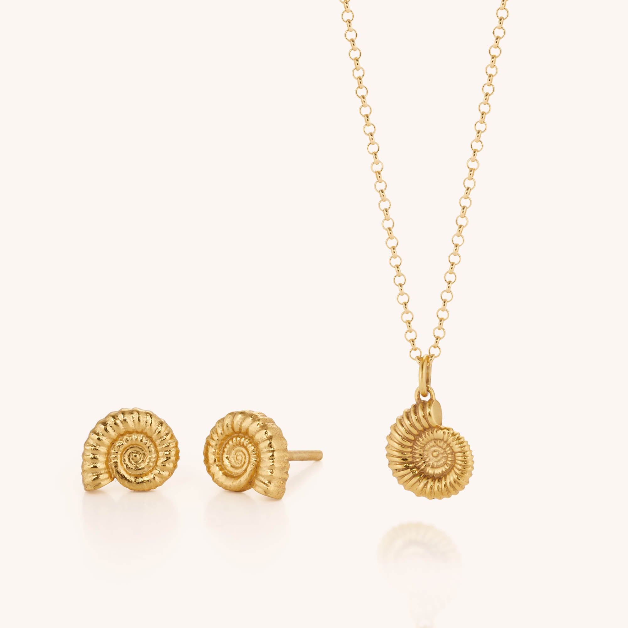 The Ammonite Necklace &amp; Earring Set, crafted in gold and sterling silver, features a detailed spiral shell design on both the necklace and matching stud earrings, all beautifully displayed on a white background.