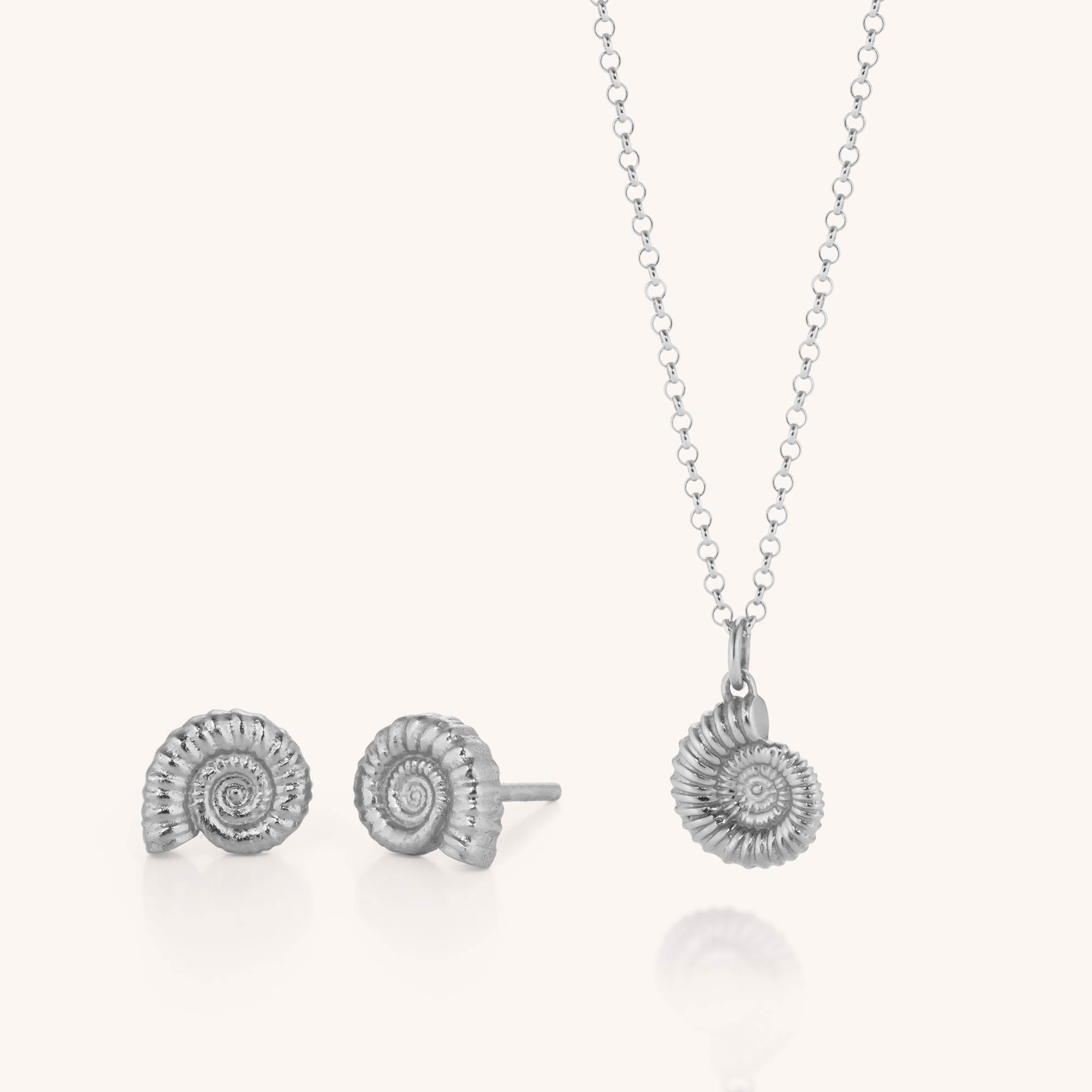 The Ammonite Necklace &amp; Earring Set showcases a pair of sterling silver spiral shell stud earrings and a coordinating fossil pendant necklace on a delicate chain, elegantly presented against a light background.