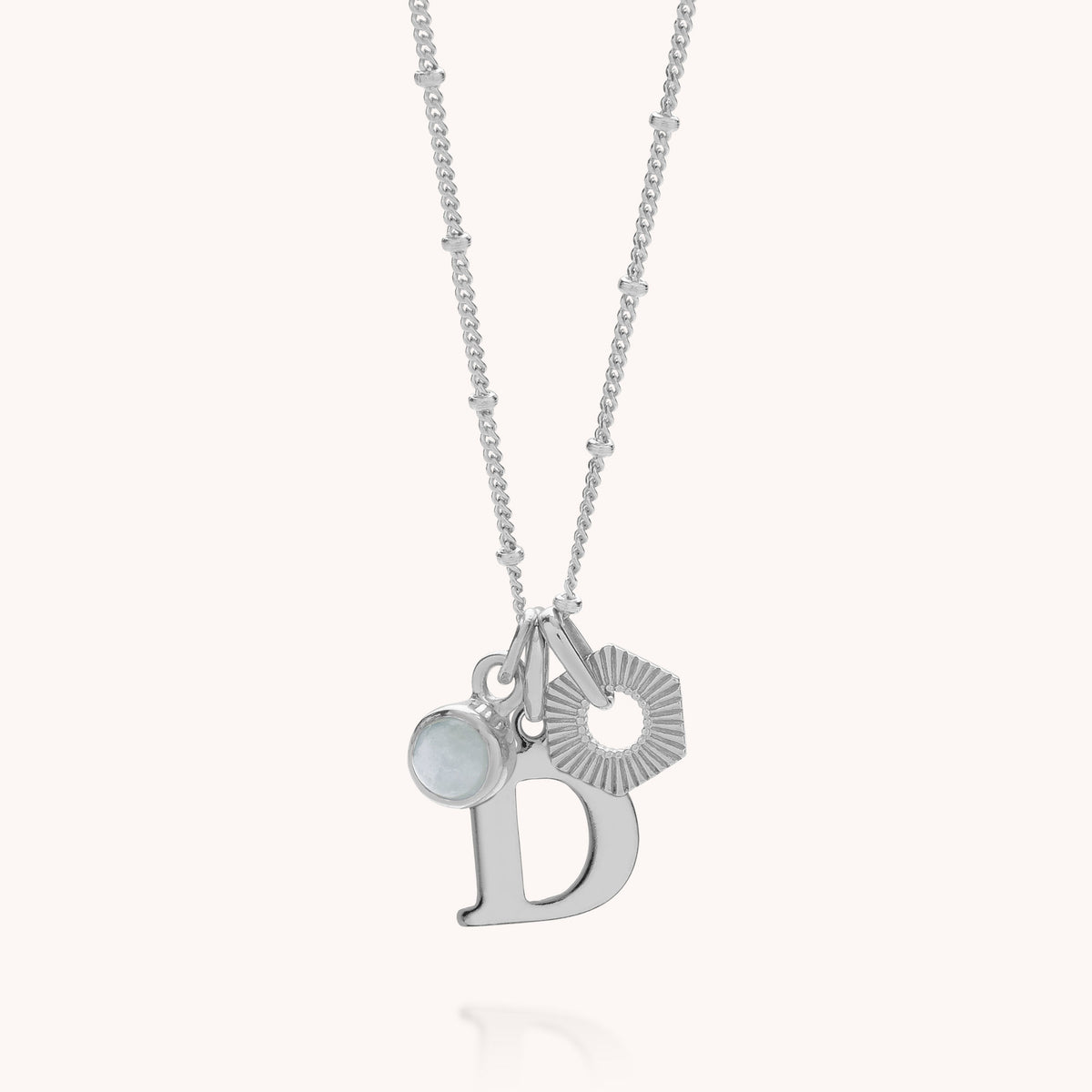 Introducing the HEX Personalised Birthstone Necklace – Sterling Silver, a beautiful piece featuring three distinctive charms: a round birthstone gemstone, a textured hexagon, and a large customisable initial D. This personalised sterling silver necklace is the perfect accessory to add a meaningful touch to any outfit.