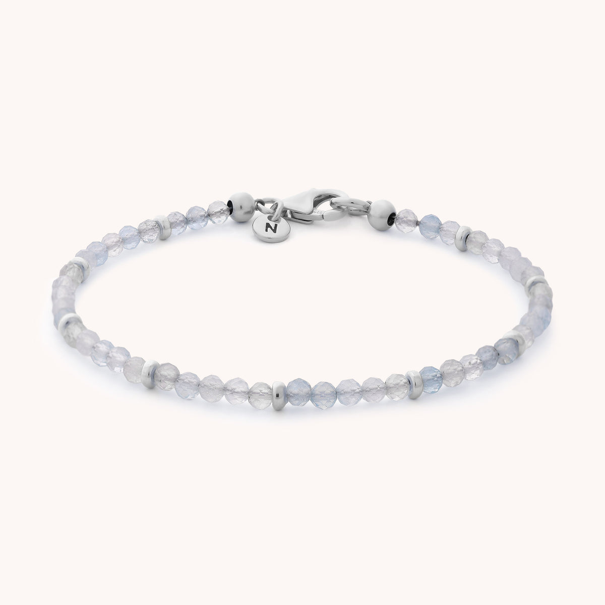 Introducing the Aquamarine Orbit Bracelet - March: This delicate bracelet features small, faceted pale blue aquamarine beads accented with silver, a secure lobster clasp, and a small round tag engraved with an initial. As the perfect March birthstone gemstone jewelry, it brings a subtle touch of elegance to any outfit.