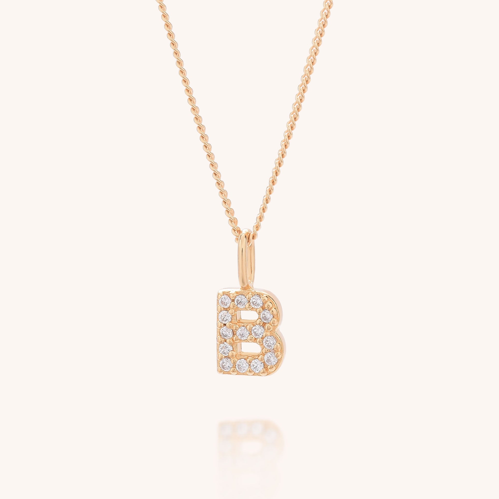 The Initial Sparkle Necklace features a gold pendant in the shape of the letter B, adorned with sparkling cubic zirconia stones and displayed on a light background.